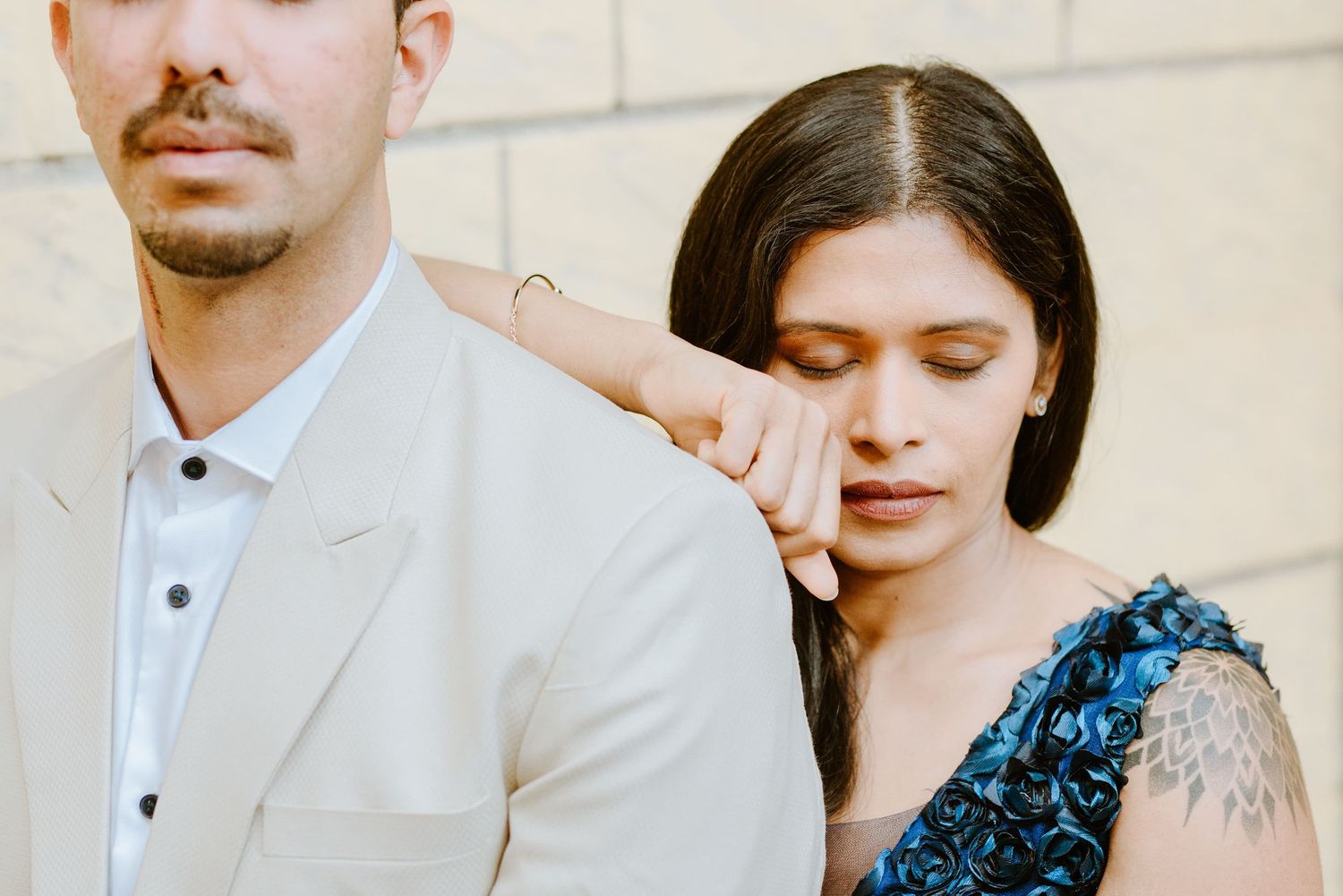 A woman in a blue floral dress rests her head on a man's shoulder in a tender, emotional moment.