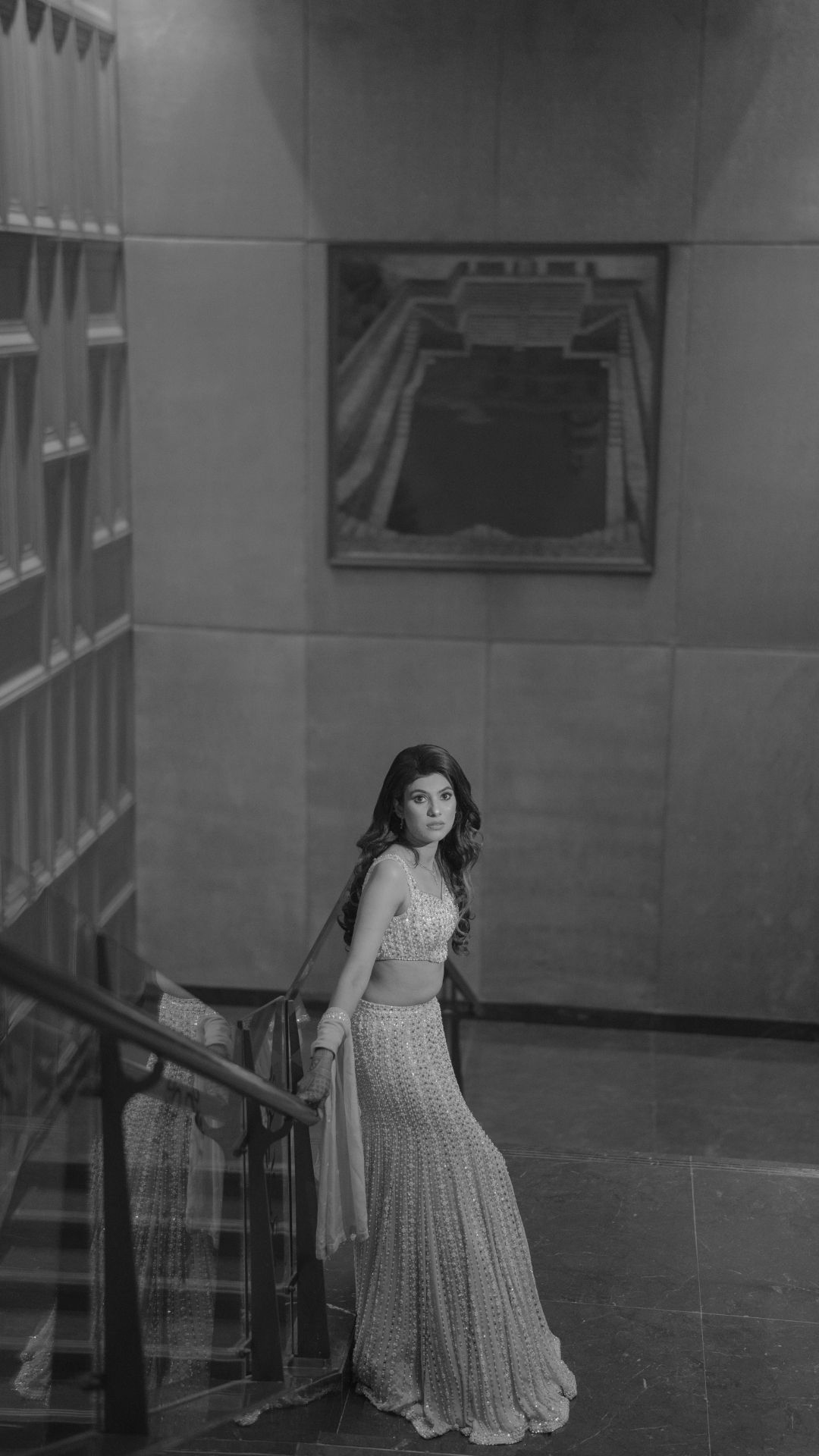 Elegant woman in a white embroidered lehenga posing on a staircase in a black and white portrait photo.