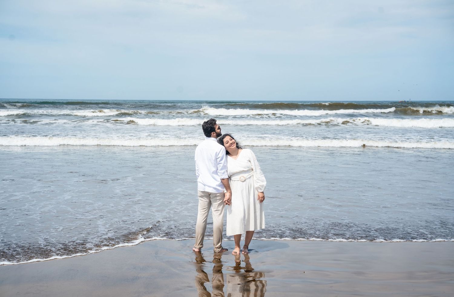 Couple walking along the shoreline as waves crash on a sunny beach day.