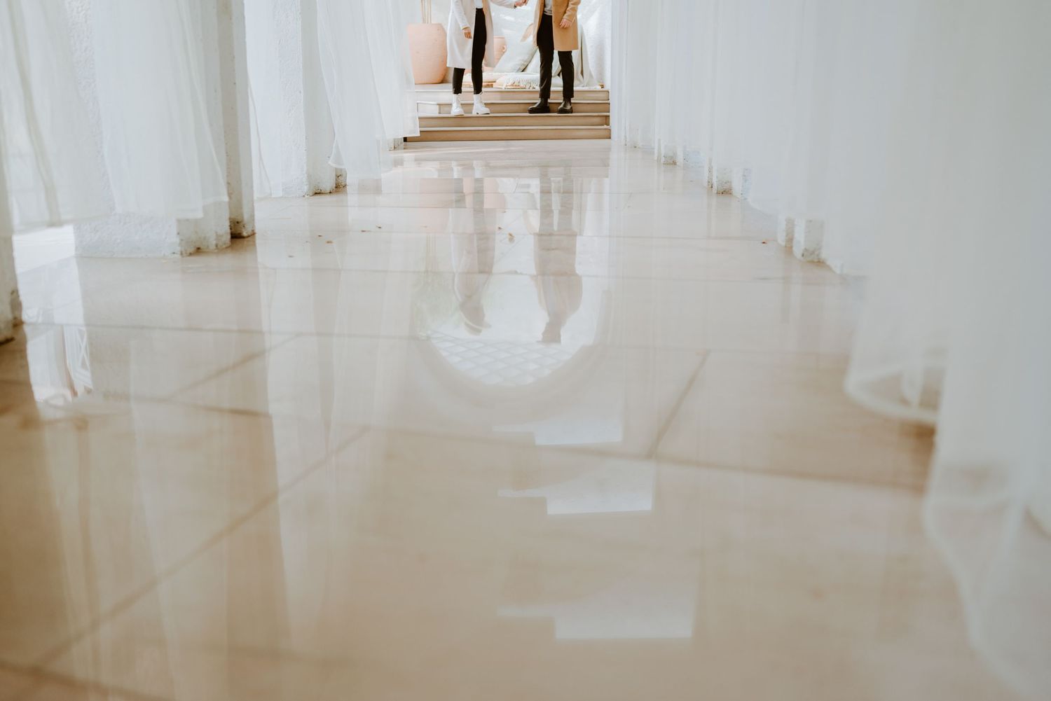 Elegant white marble hallway with reflective floors and tall columns, featuring two people standing in the background.