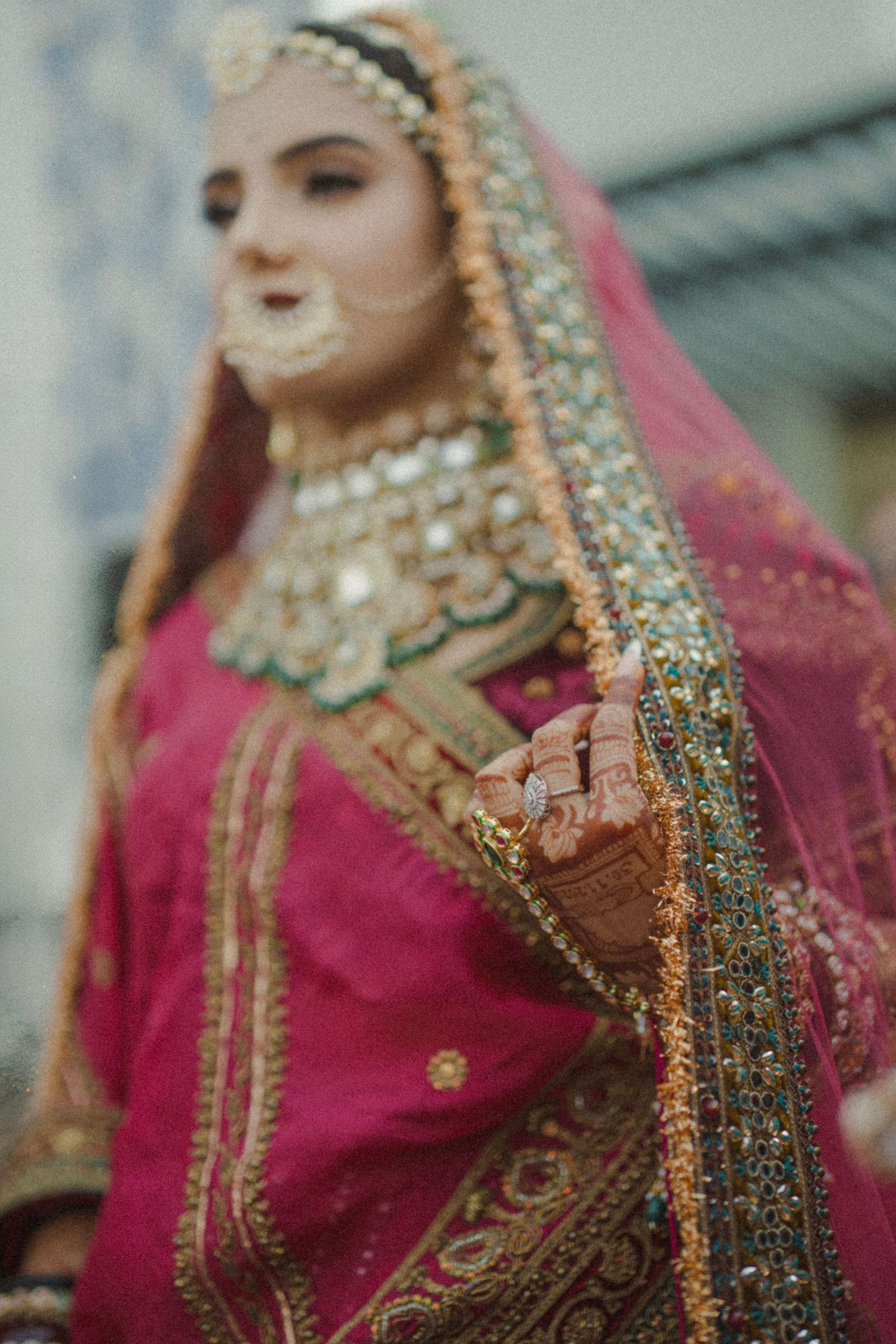 Bride in pink lehenga with gold embroidery, kundan jewelry, and mehndi hands, wearing a dupatta veil.