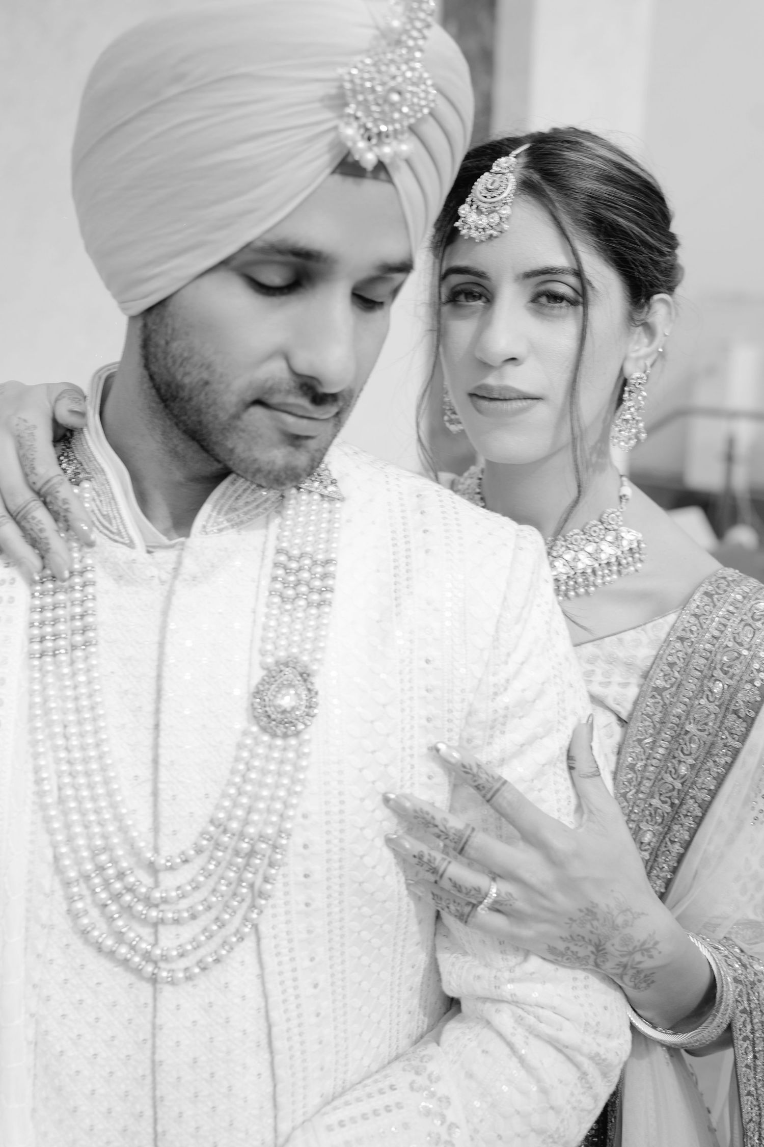 Black and white photo of a Sikh couple in traditional wedding attire, groom in turban with pearl necklace, bride in embroidered dupatta.