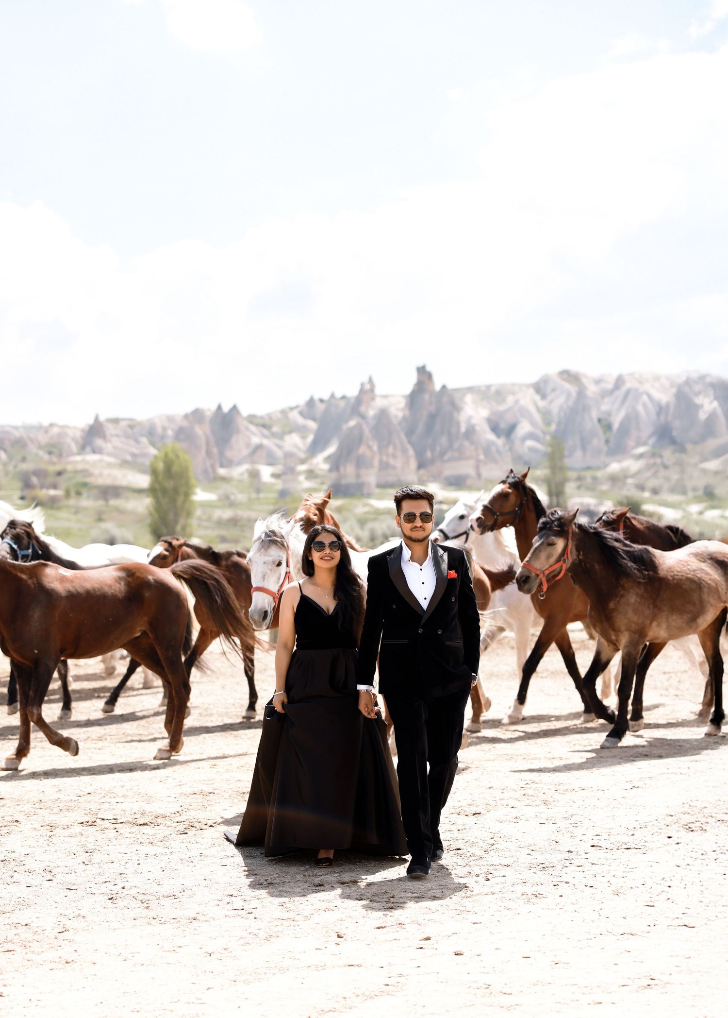 A couple poses with wild horses in the desert landscape while taking wedding photos.