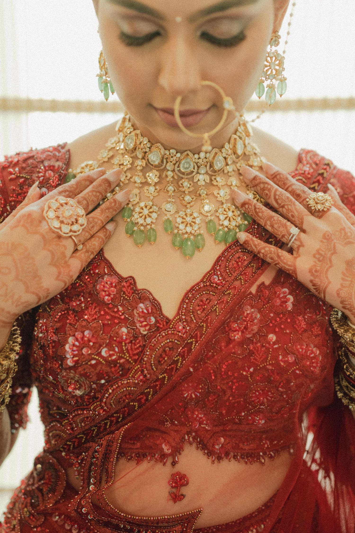 Close-up of traditional Indian bridal jewelry and red lehenga with intricate henna designs on hands.