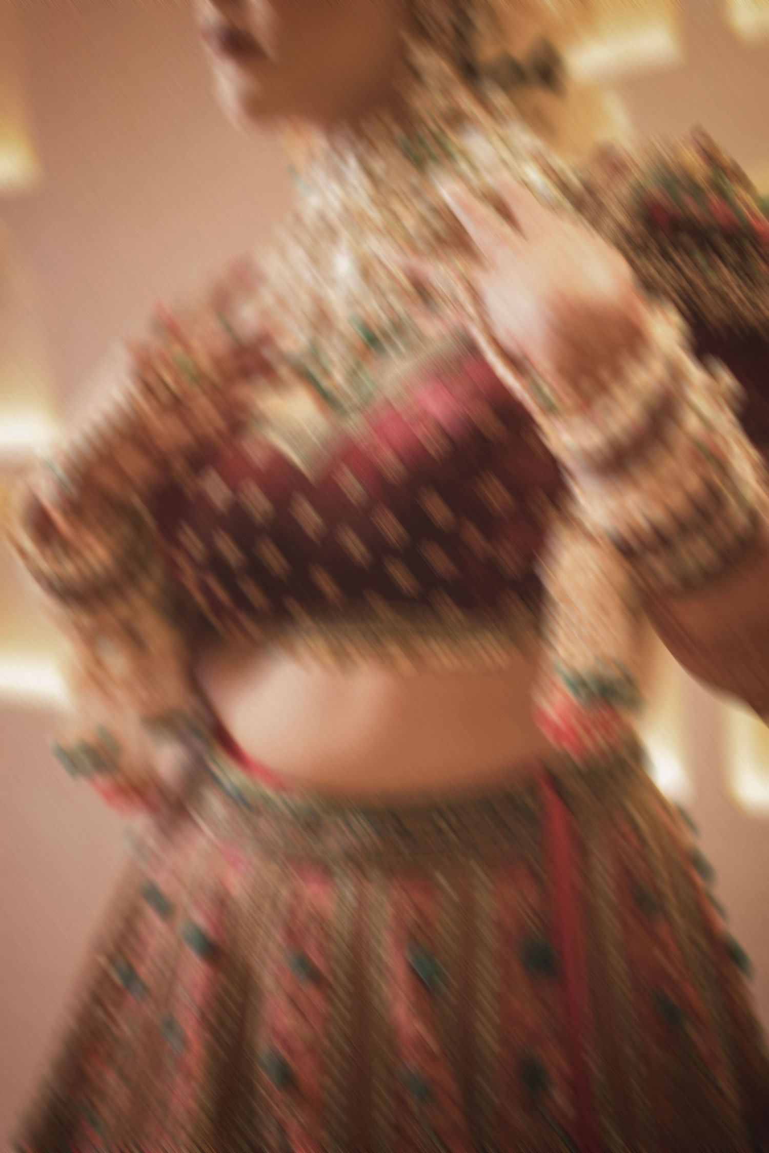 Blurred photo of a woman wearing a colorful embroidered Indian lehenga choli with gold bangles and decorative lights.