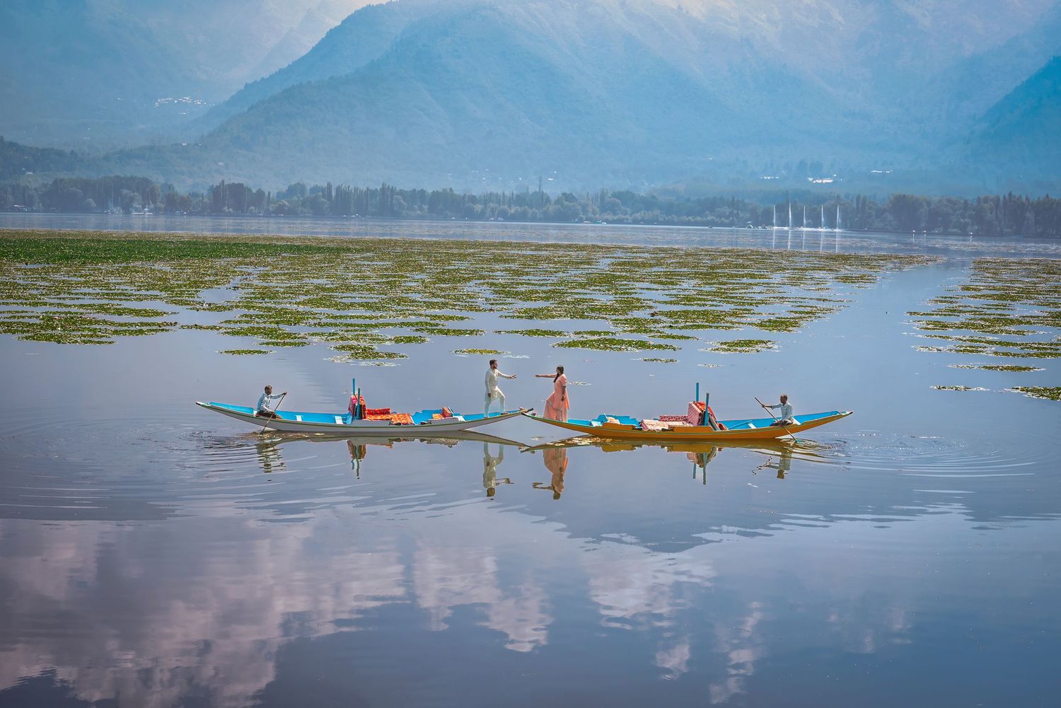 Colorful kayakers paddling across a serene mountain lake with reflections in the calm water.