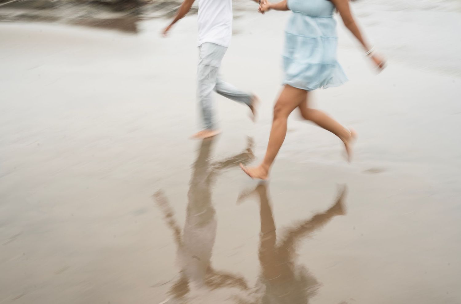 Two people running and splashing in shallow beach water at sunset.