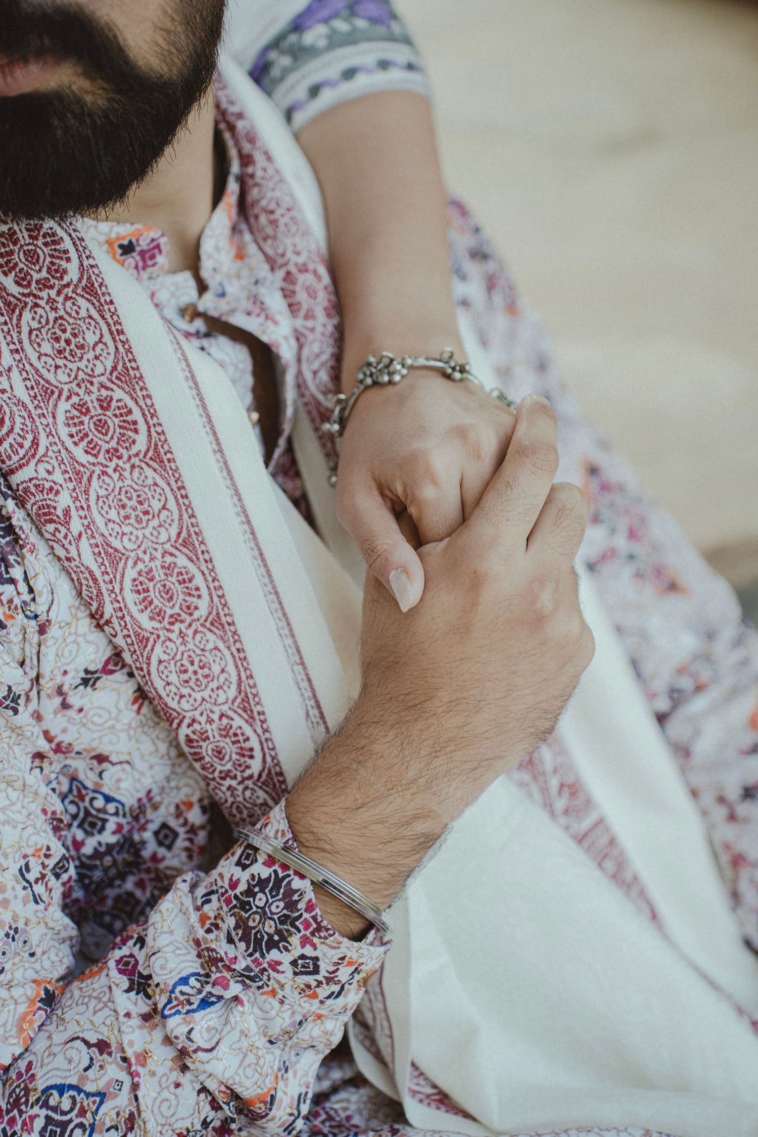 Close-up of a couple holding hands, wearing traditional patterned ethnic attire with silver bracelets.