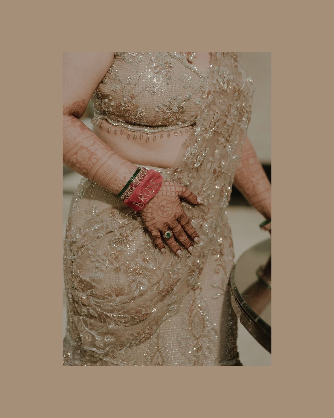 A bride wearing a beige embellished saree with intricate mehndi on her hands and red bangles with rings.