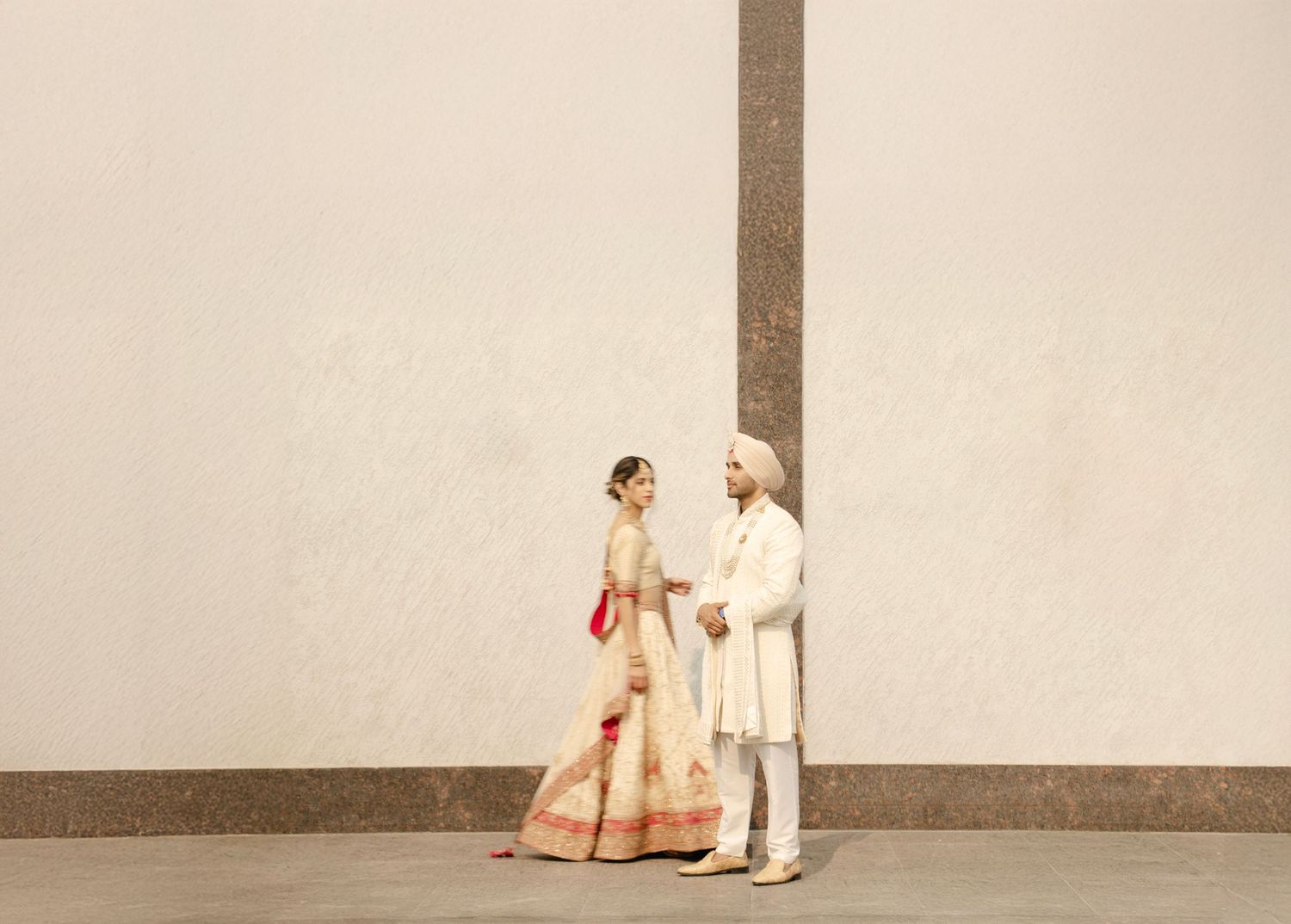 Indian couple in traditional wedding attire holding hands, bride in red lehenga and groom in white sherwani.