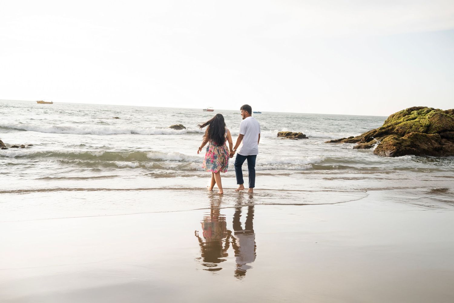 Couple walking along a scenic rocky beach coastline at sunset.