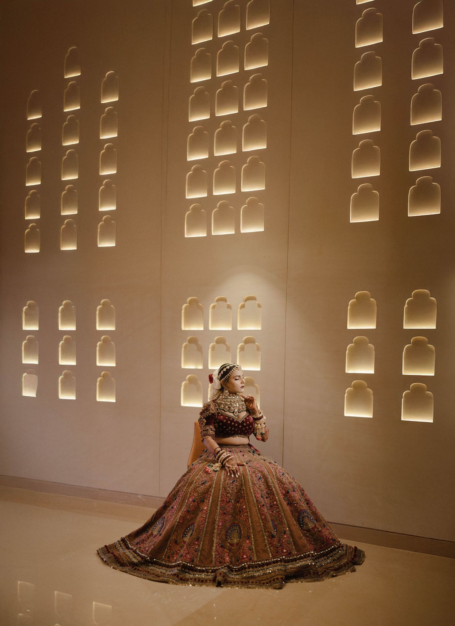 Brown dress with intricate patterns displayed in a gallery space with illuminated wall niches creating dramatic lighting.