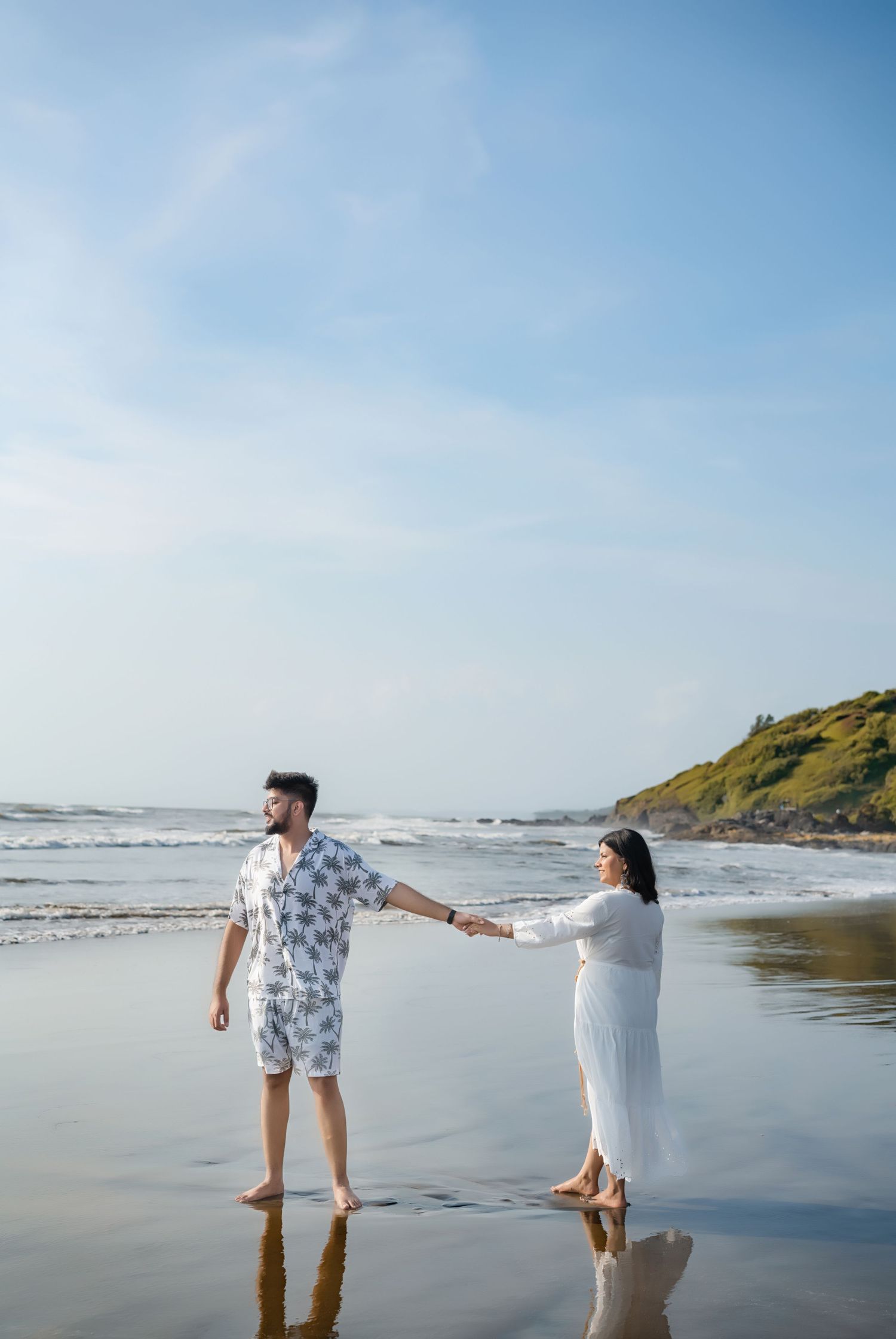 Couple walking and playing along a scenic beach shoreline during low tide.