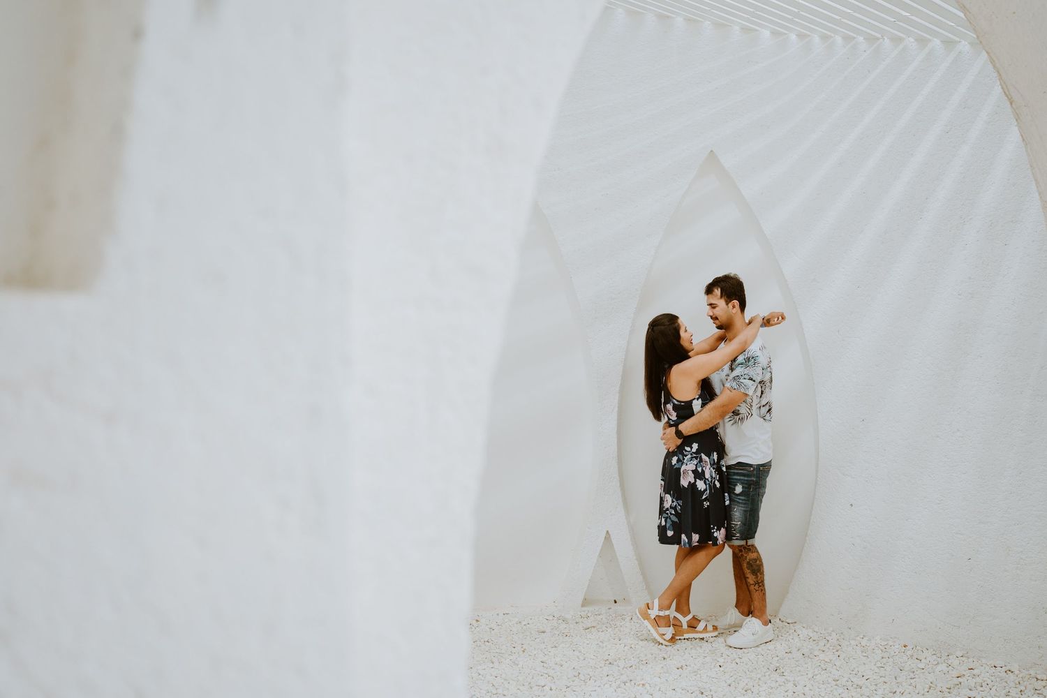 Couple embracing romantically in a stunning white architectural archway, perfect for engagement or wedding photography inspiration.