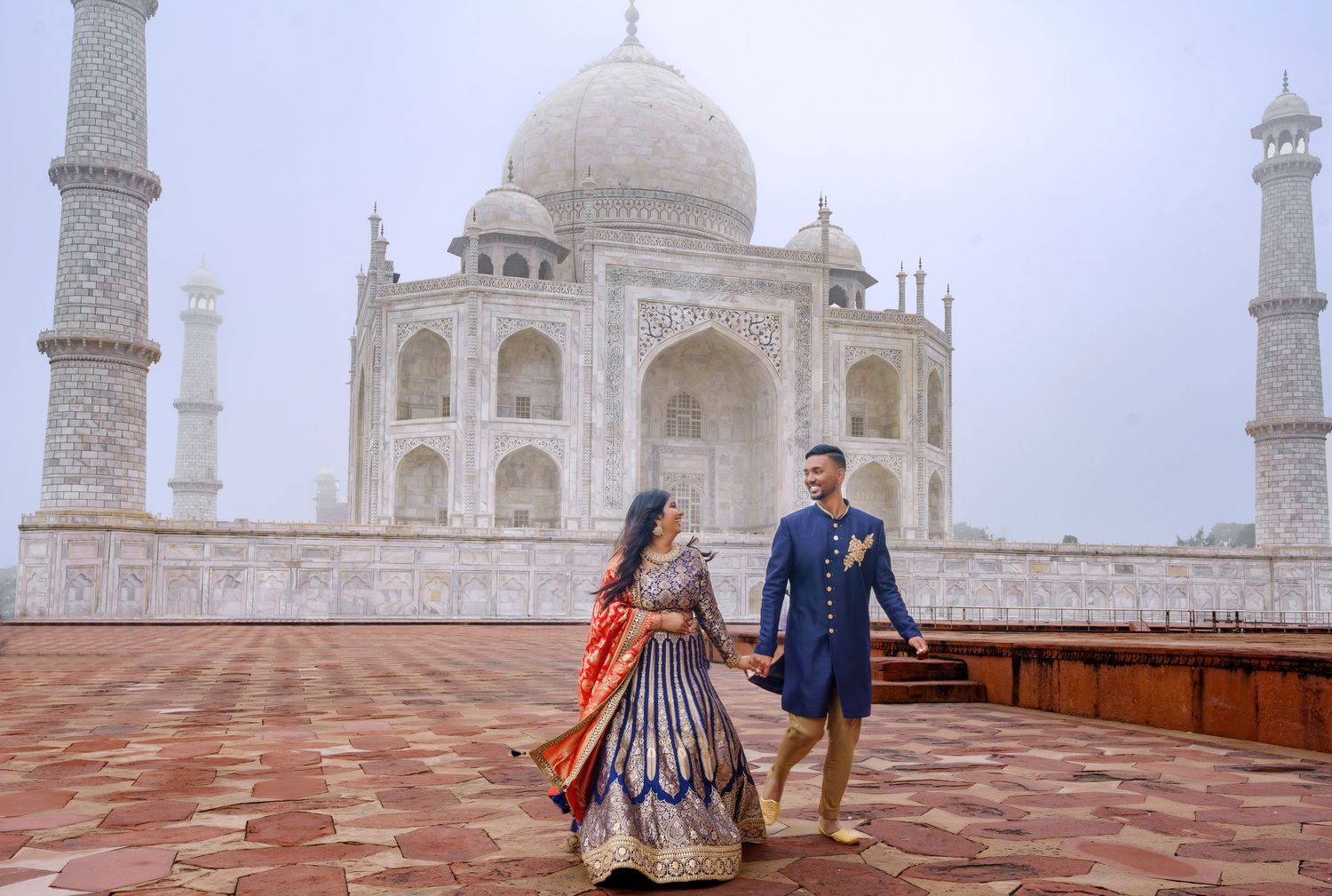 Misty view of the Taj Mahal with its iconic domes and minarets against cloudy sky.