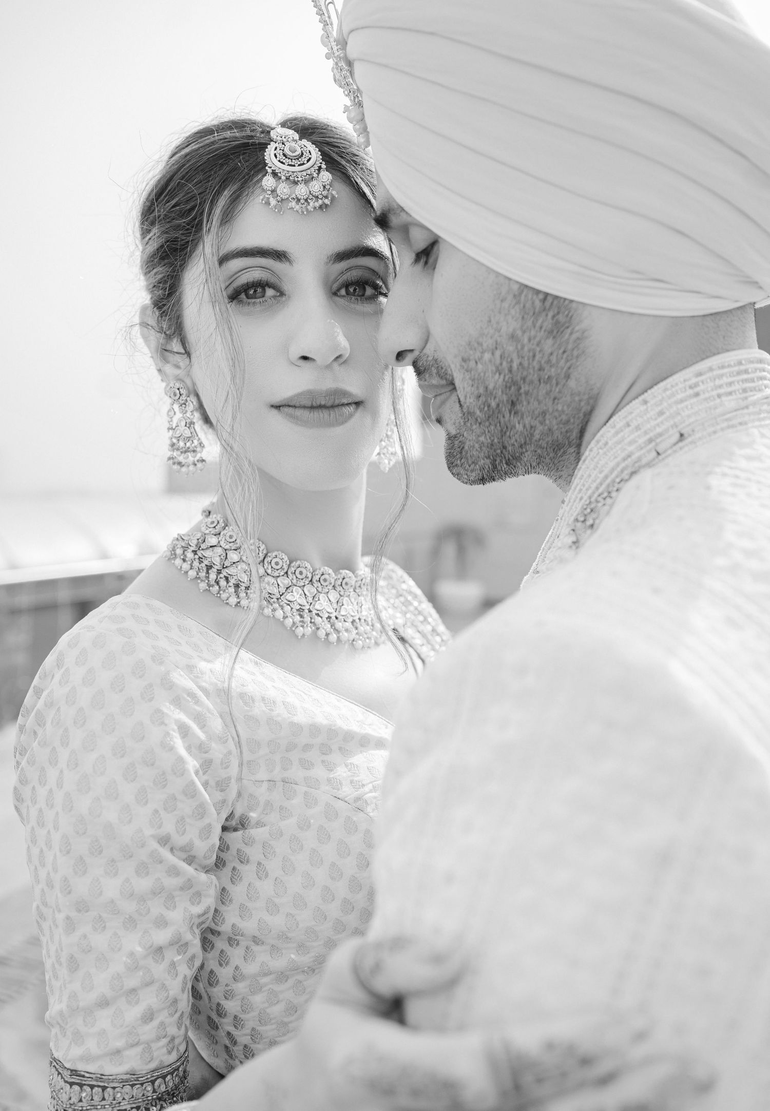 Black and white photo of a Sikh bride in traditional jewelry and groom in turban at their wedding ceremony.