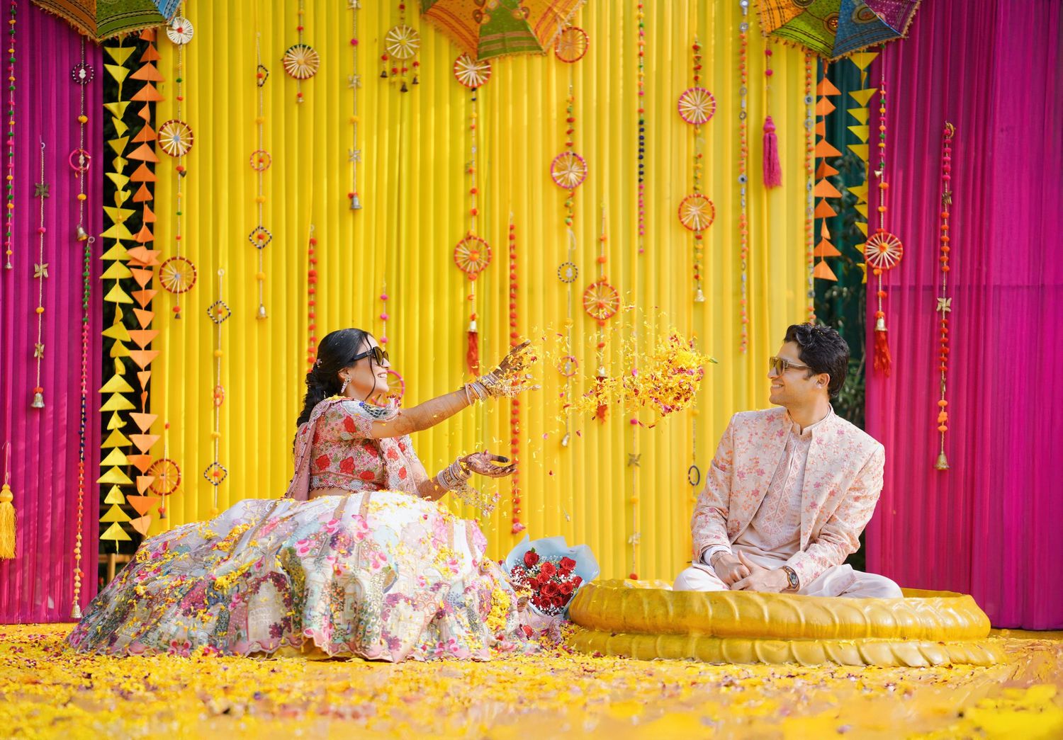 Festive Indian wedding ceremony with vibrant yellow and pink decor featuring floral arrangements and traditional elements.