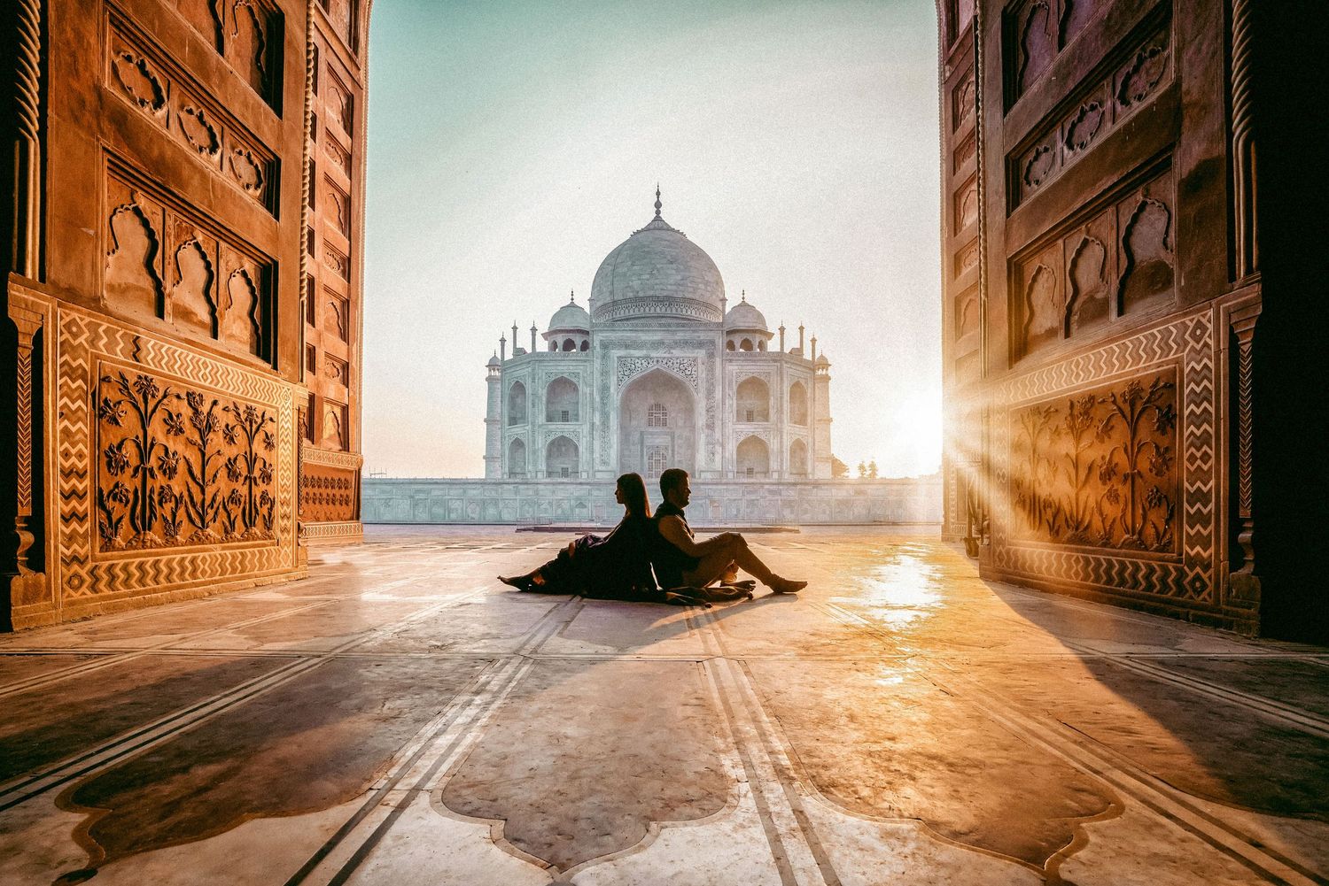 Serene sunrise view of the Taj Mahal through ornate archways with dramatic golden light.
