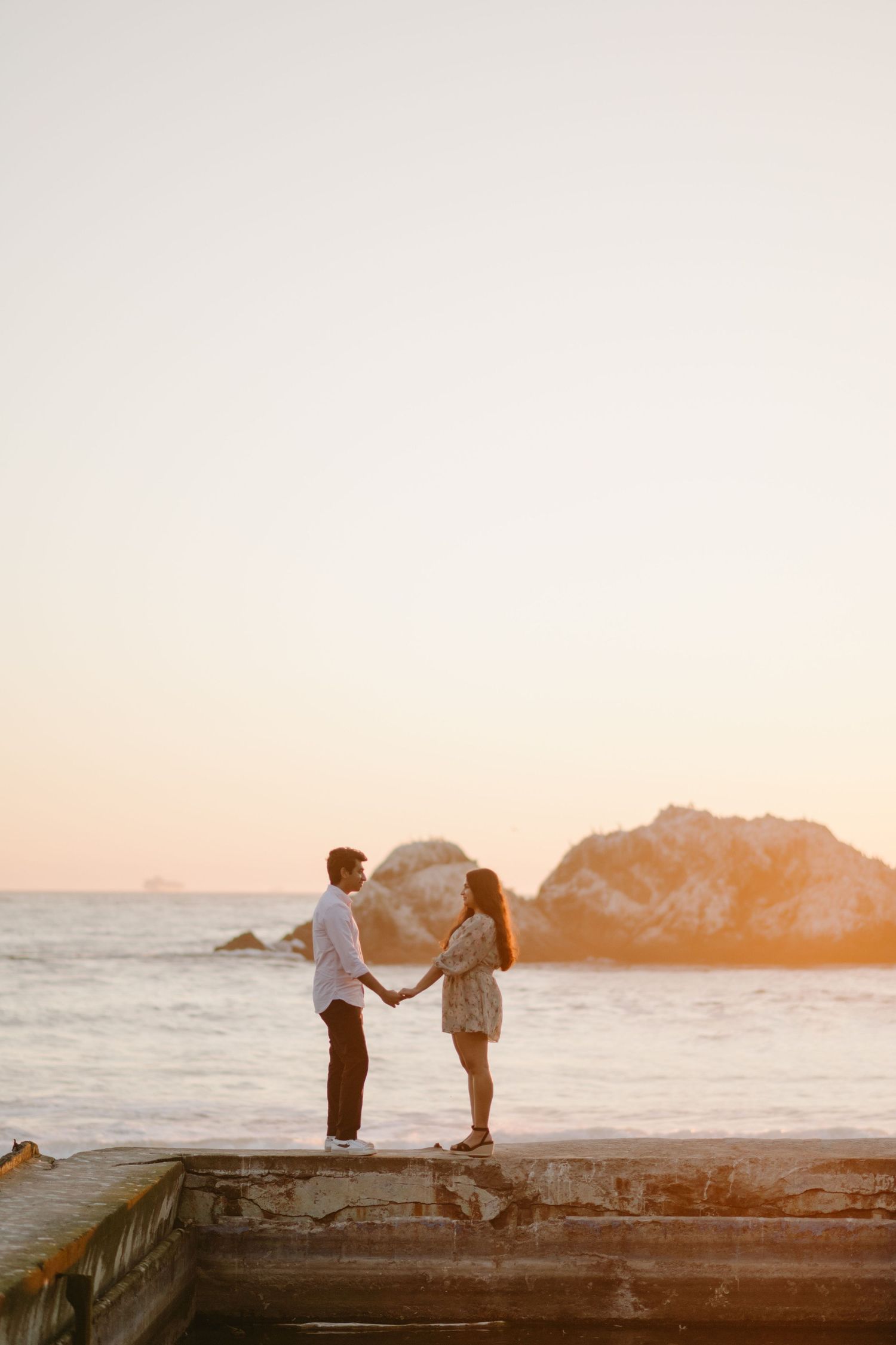 Silhouetted couple stands on rocky coastline during golden hour.