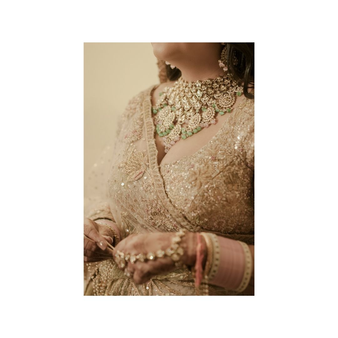Bride in cream embellished lehenga with ornate gold and diamond choker necklace and matching bangles.