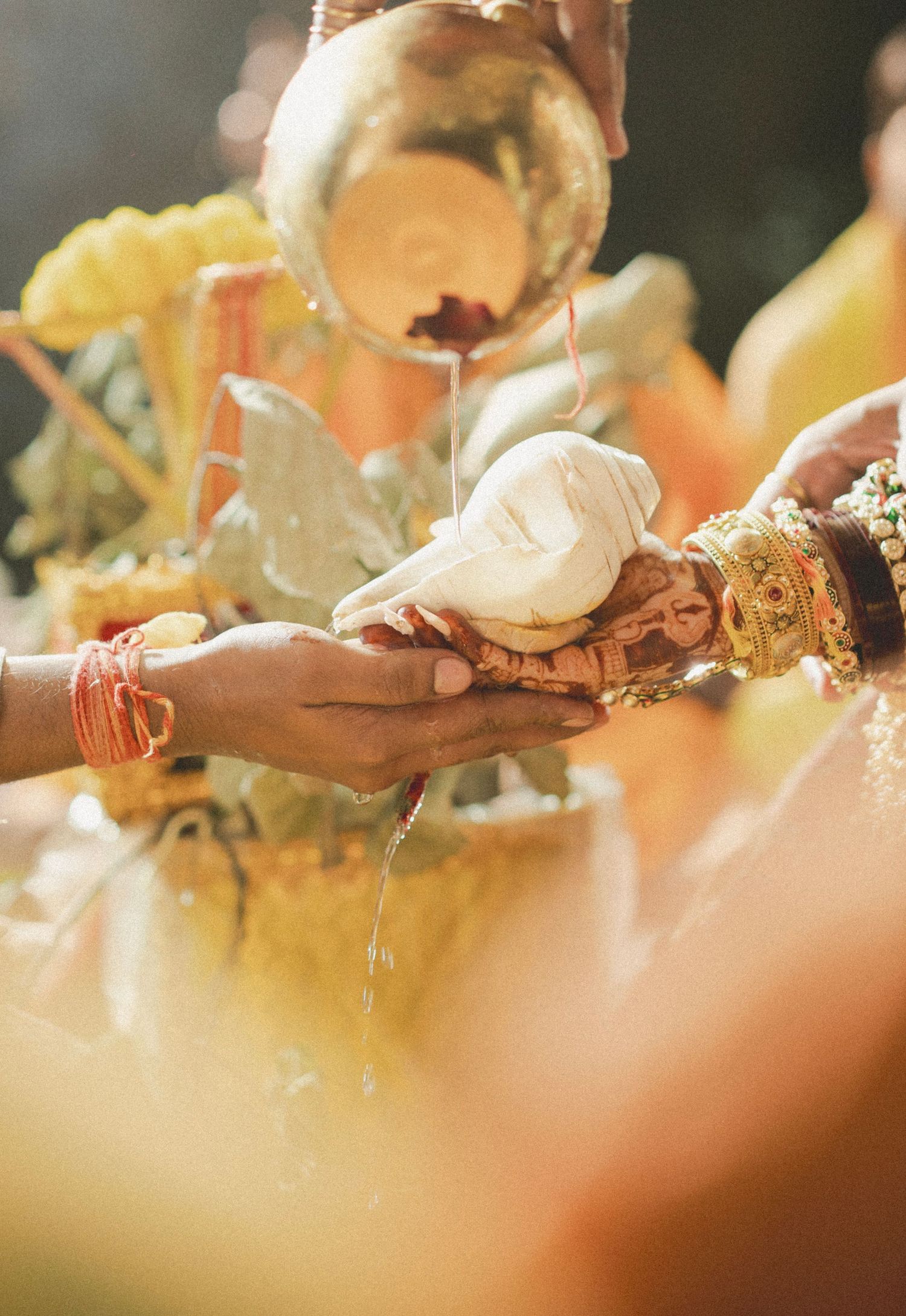 Water being poured over joined hands during a traditional Hindu wedding ceremony with gold jewelry and red bangles.