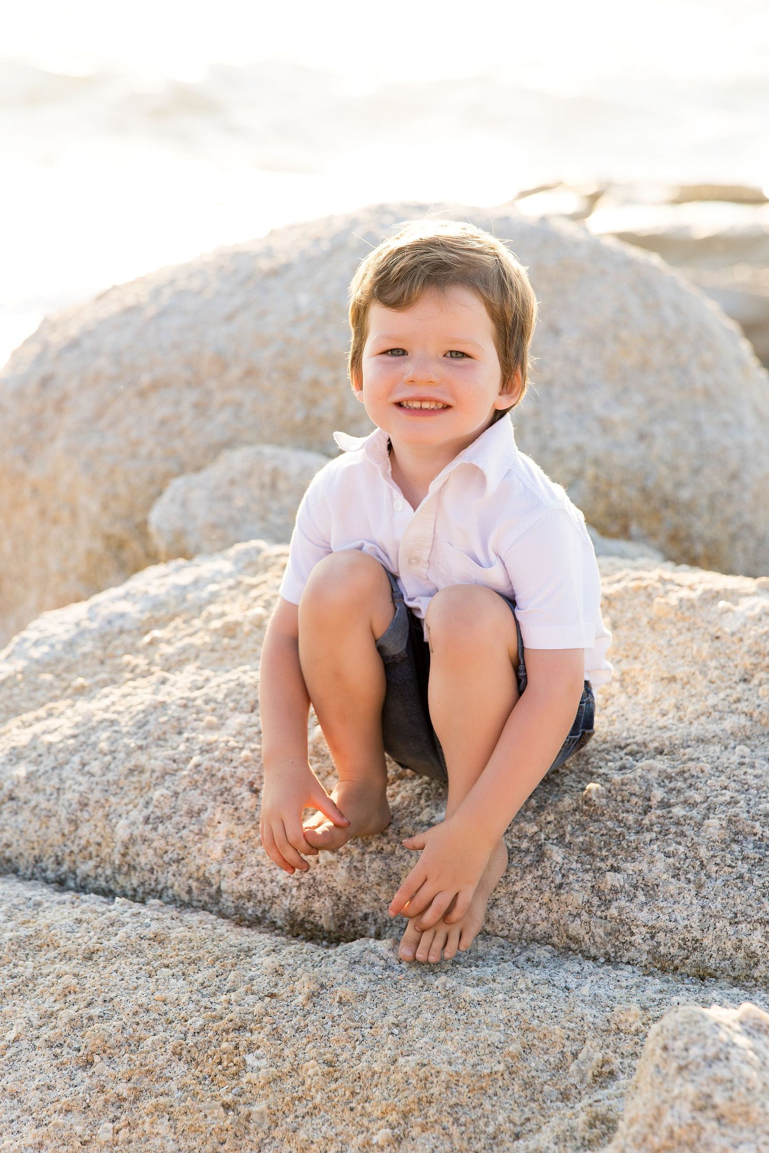 Child sitting cross-legged on large granite boulder at beach.