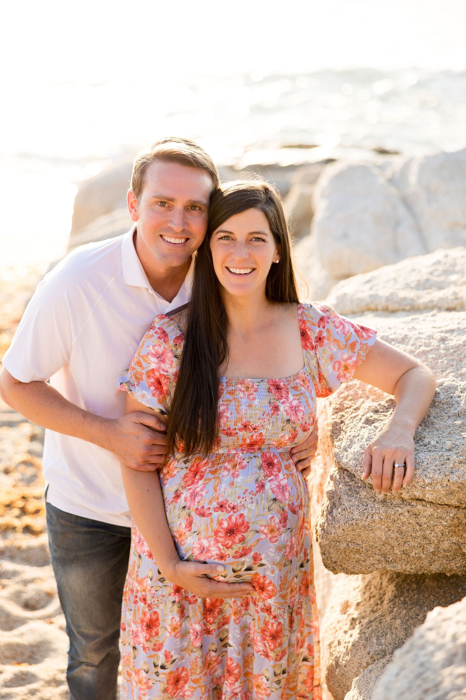 Couple sharing intimate moments on rocky beach during golden hour photography session.