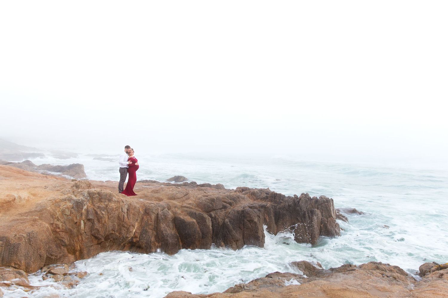 A rocky coastal landscape with crashing waves and rugged cliffs stretches along the shoreline at sunset.