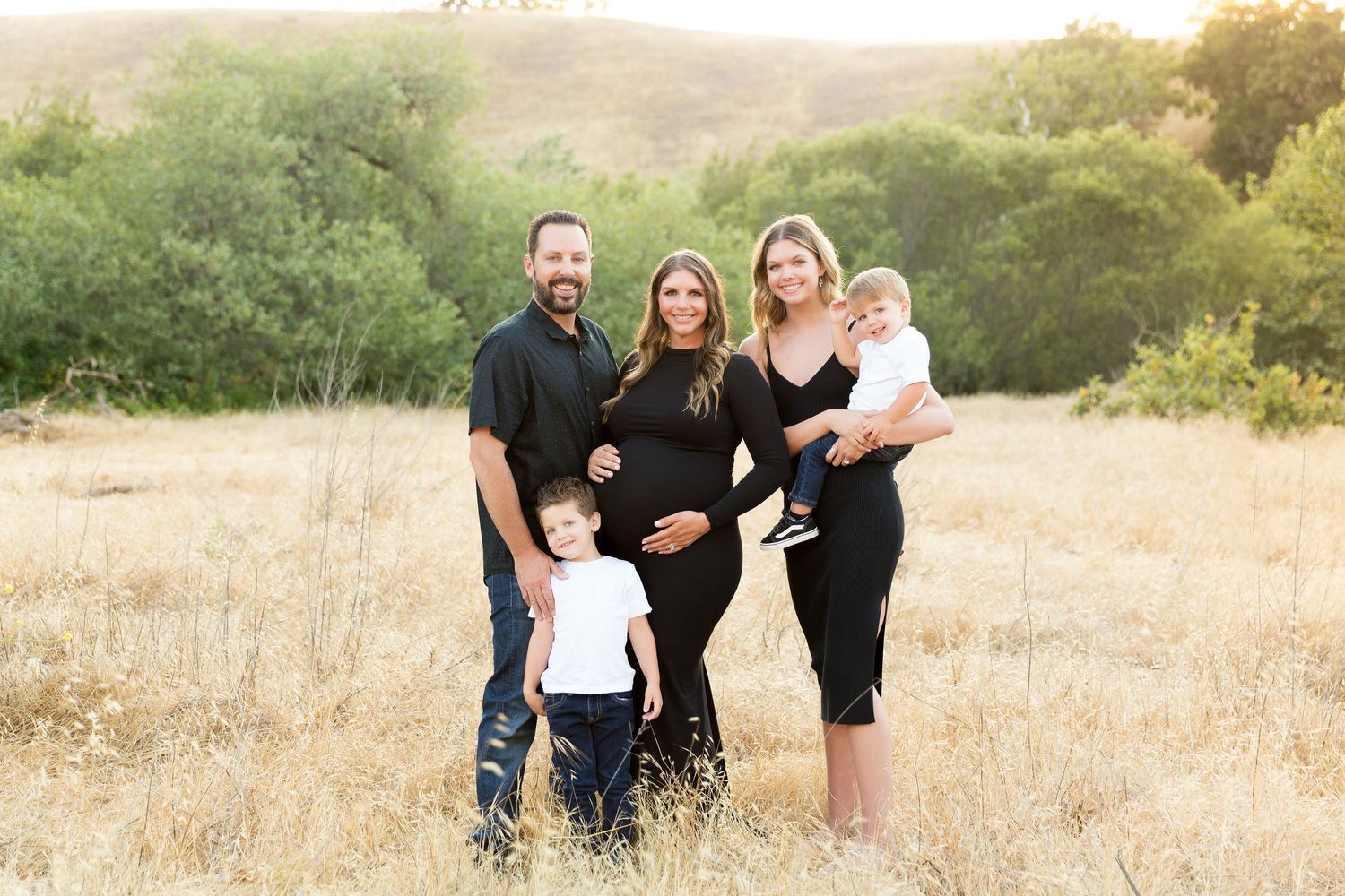 Family outdoor photo session in a golden grass field during sunset.