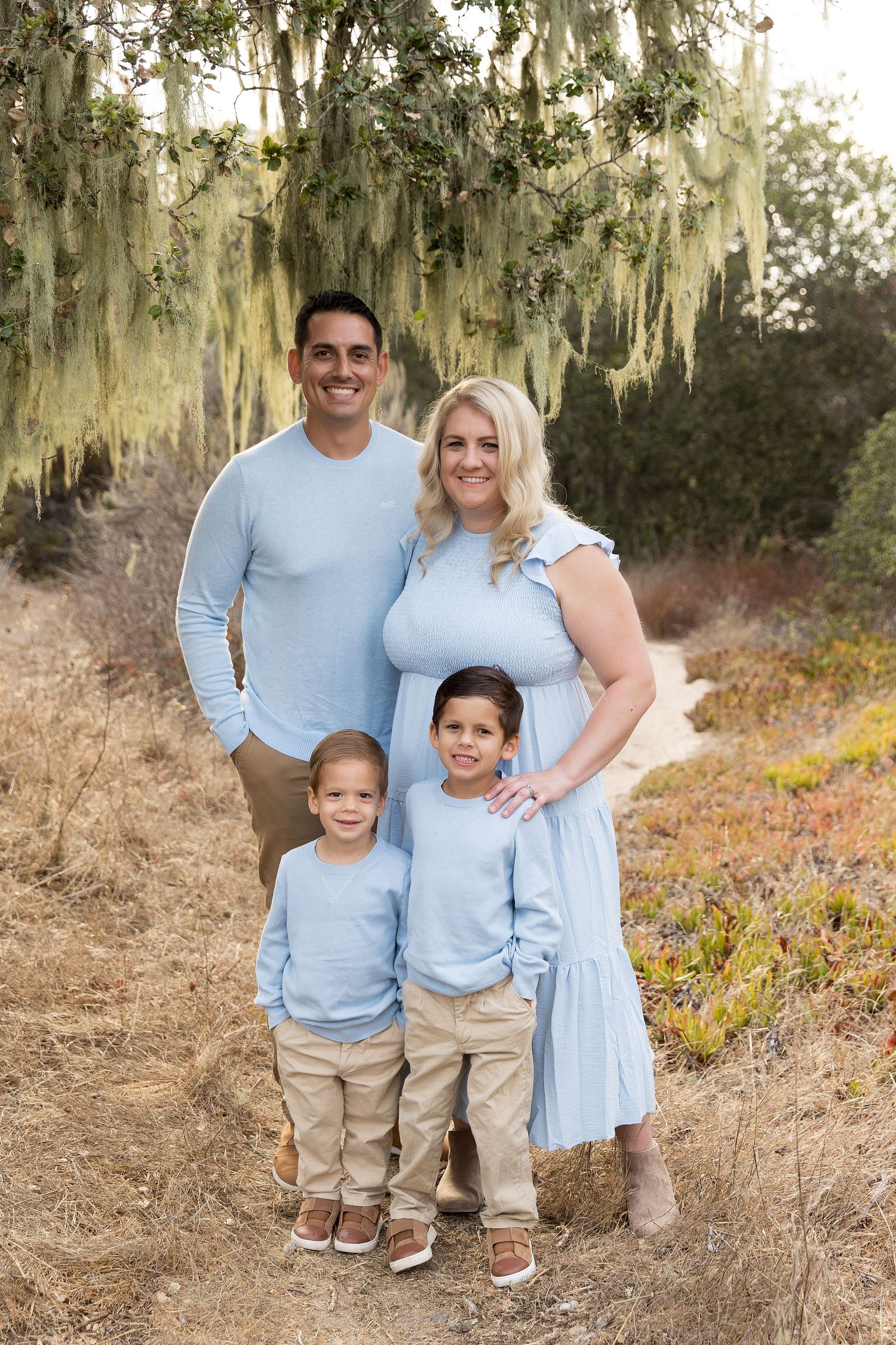 Family portrait under Spanish moss trees wearing coordinated light blue and khaki outfits.