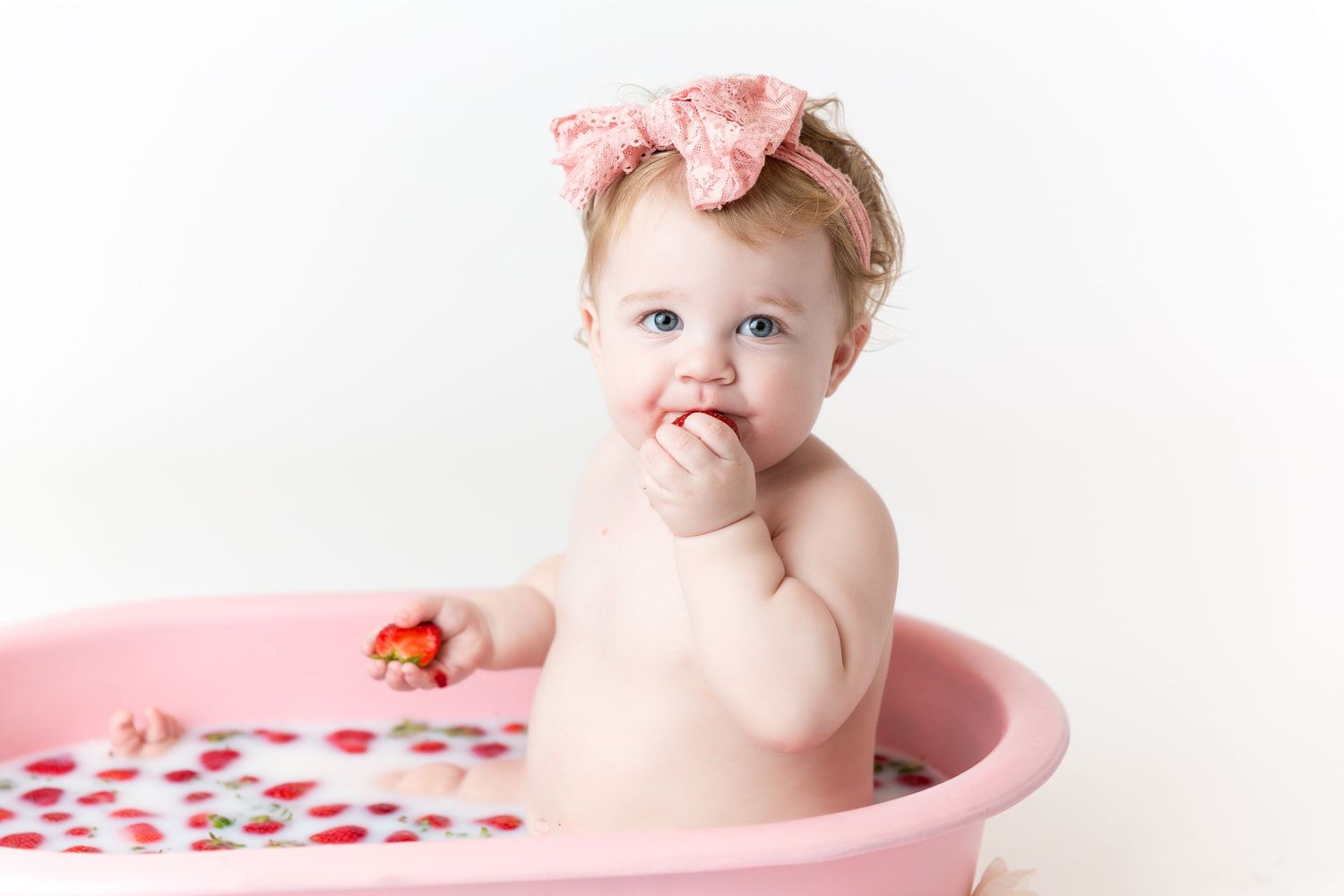 Sweet baby bath photography session in pink tub with strawberries and floral decorations.