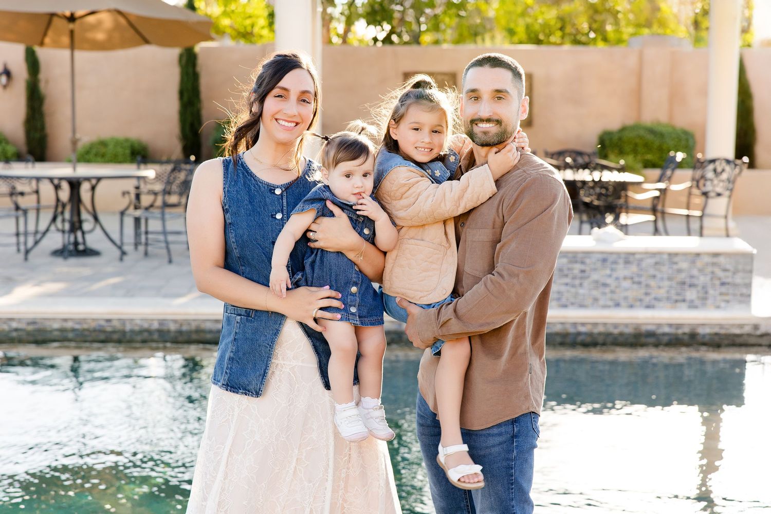 Family with young children posing by a poolside pergola during a Hollister family photo session.
