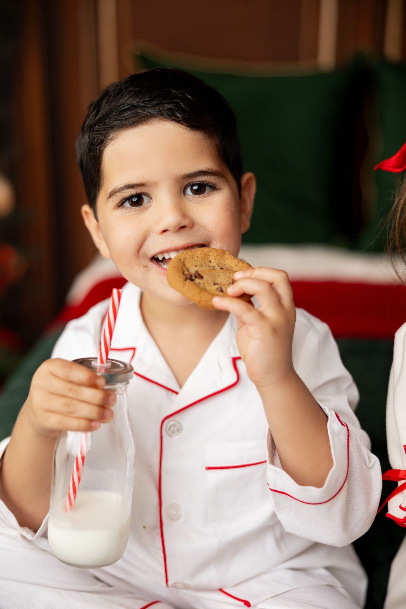 Boy in white Christmas pajamas eating a cookie with a bottle of milk at a holiday mini session in Pacific Grove