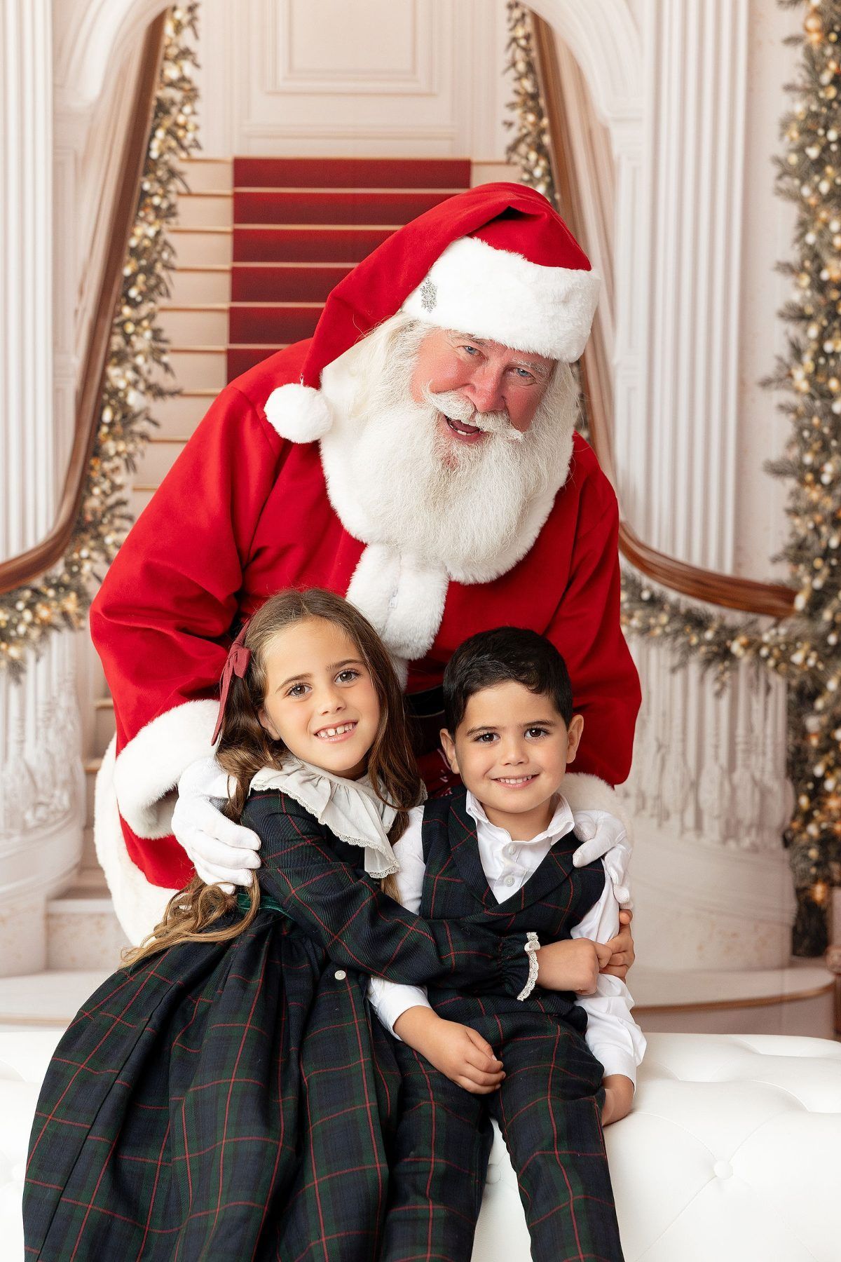 Siblings in Christmas plaid hugging in front of Santa, Pacific Grove Christmas photographer