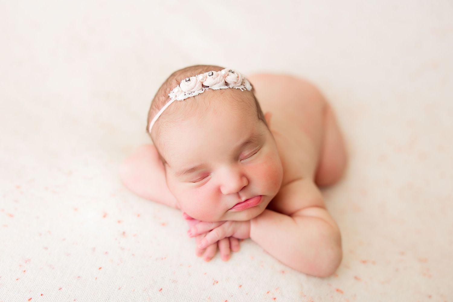Sleeping newborn with lace headband on pink and white backdrop.