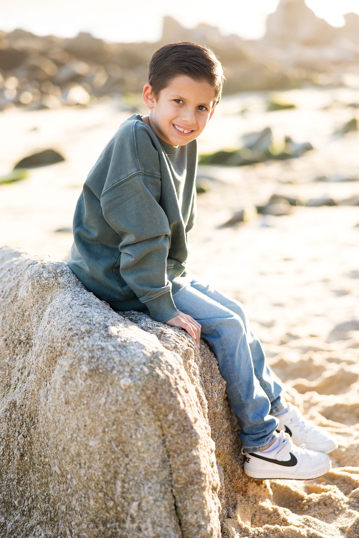 A series of casual portraits sitting on coastal rocks wearing a dark sweater.