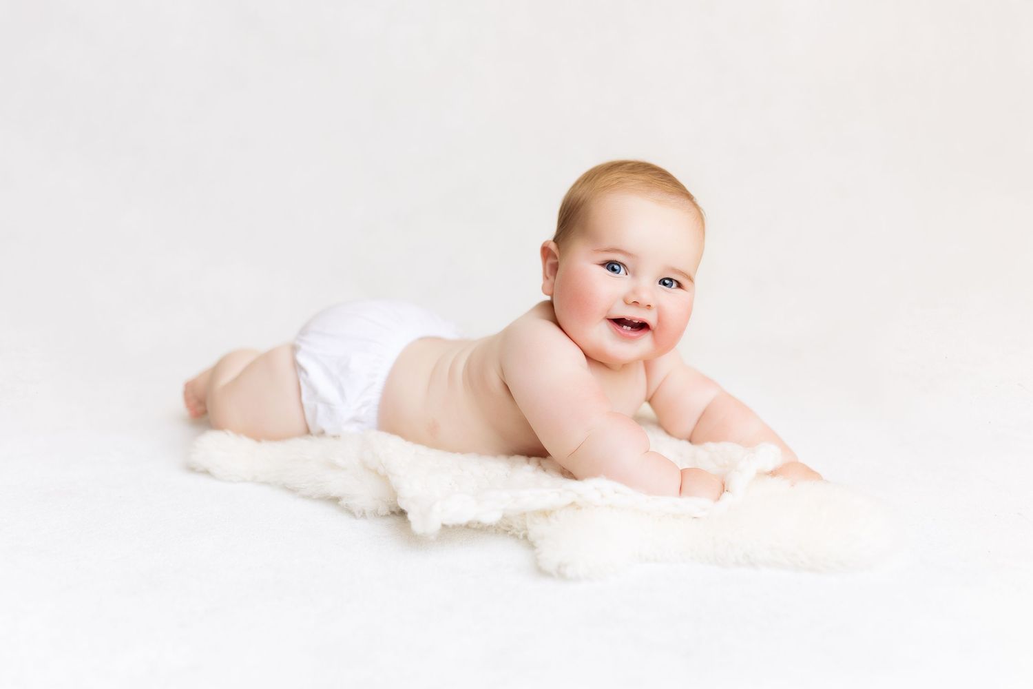 Happy baby in white diaper crawling on soft white blanket.
