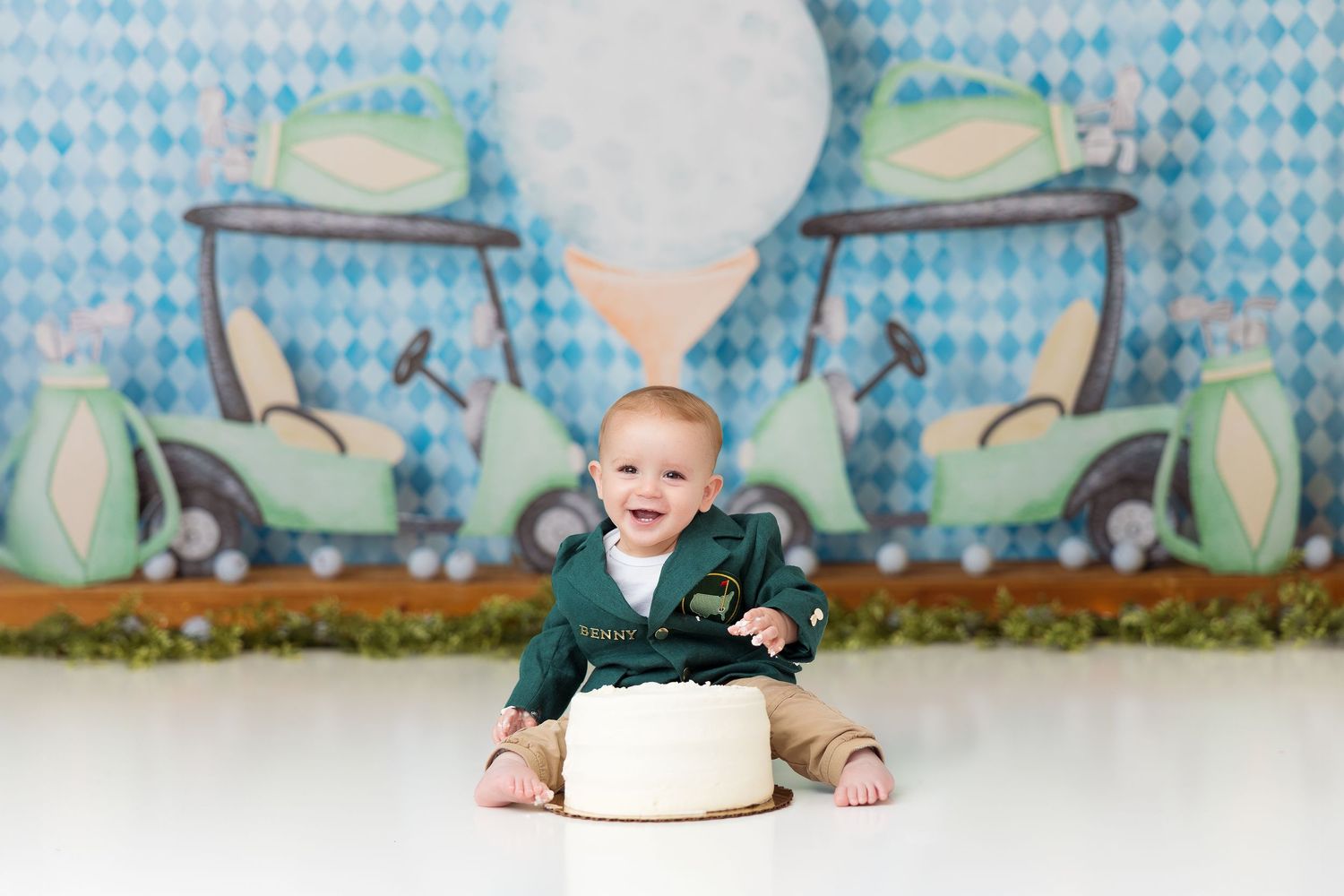 Baby with green hat sits against blue patterned backdrop during milestone photo session.