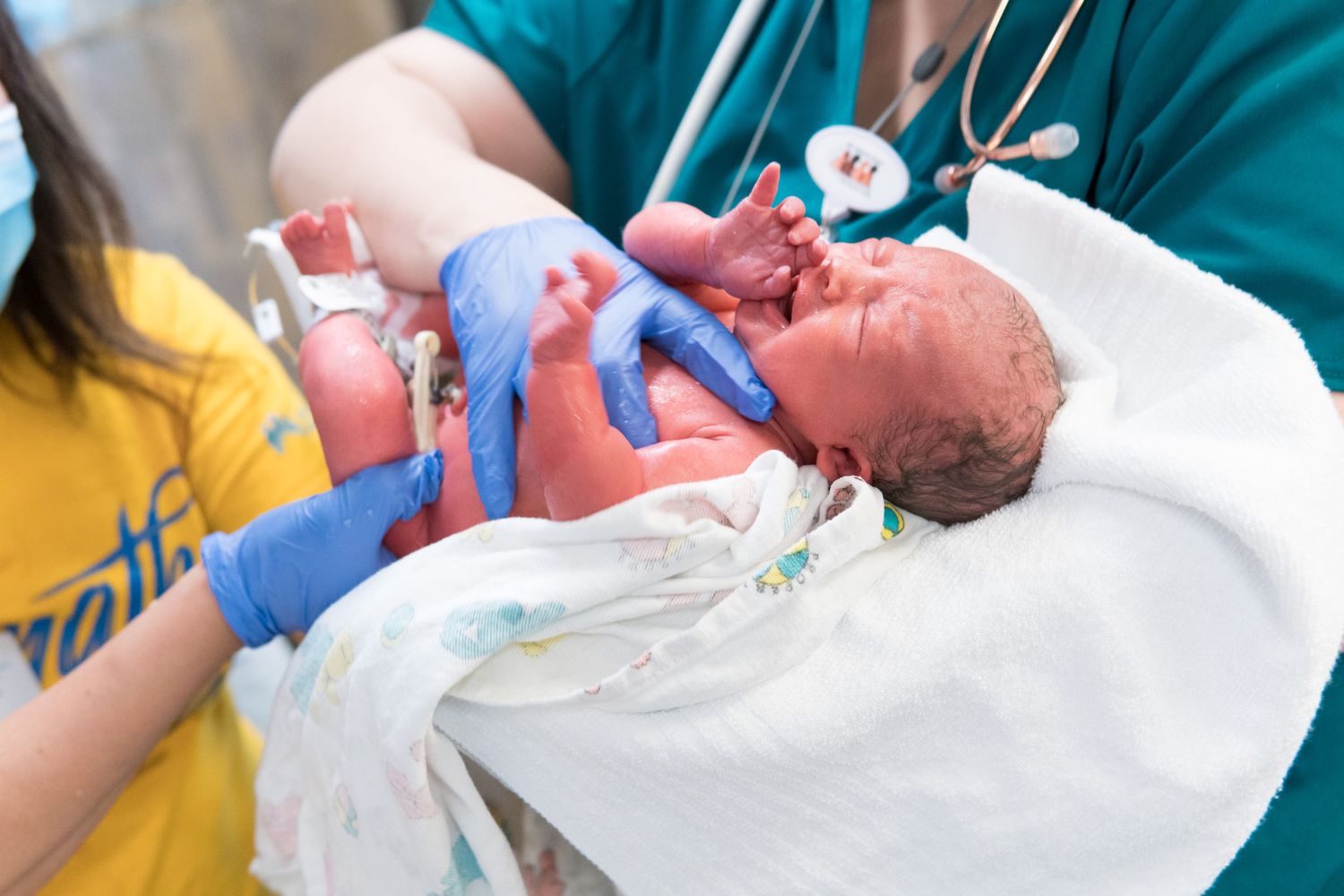 Healthcare providers in teal scrubs attending to a newborn in a medical setting.