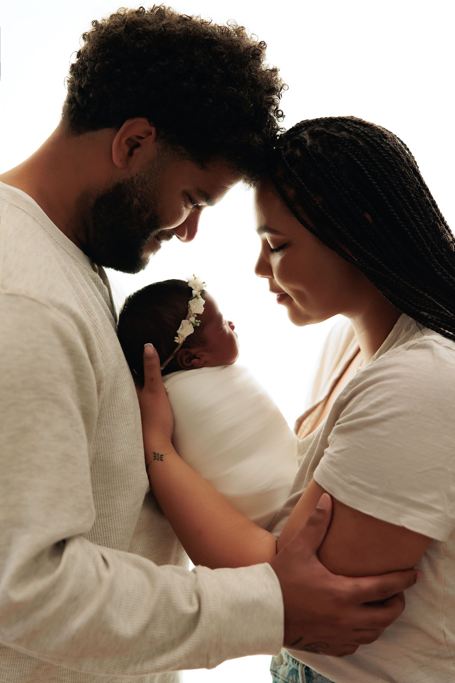 Studio portrait of parents holding their newborn baby girl, backlit with soft white light and emotional connection