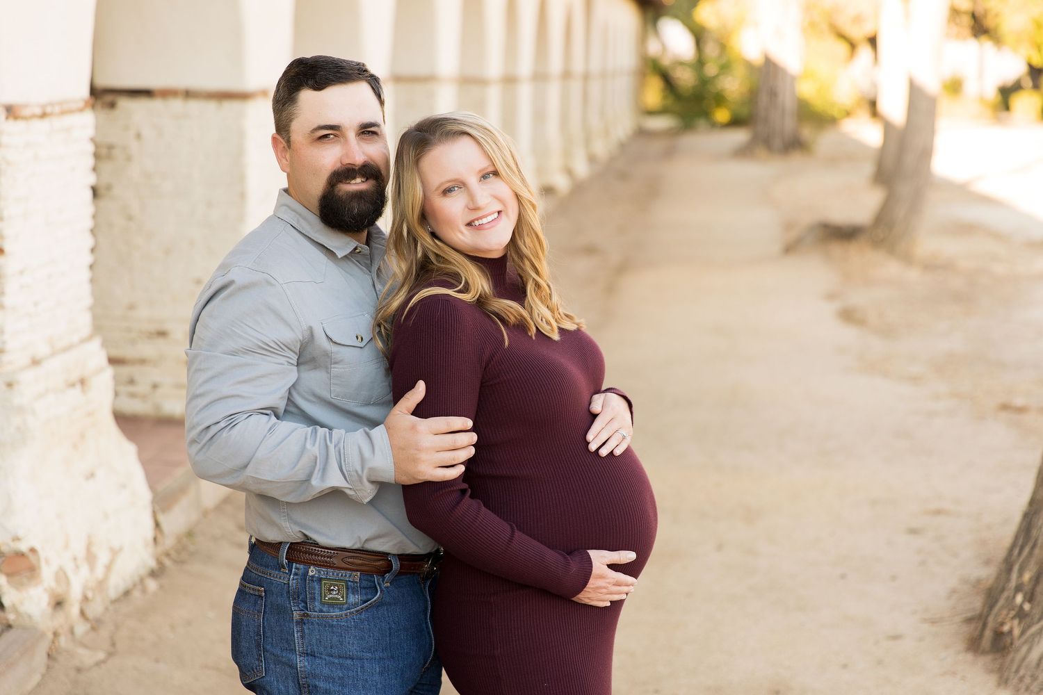 Expecting couple poses together in archway during sunset maternity session.