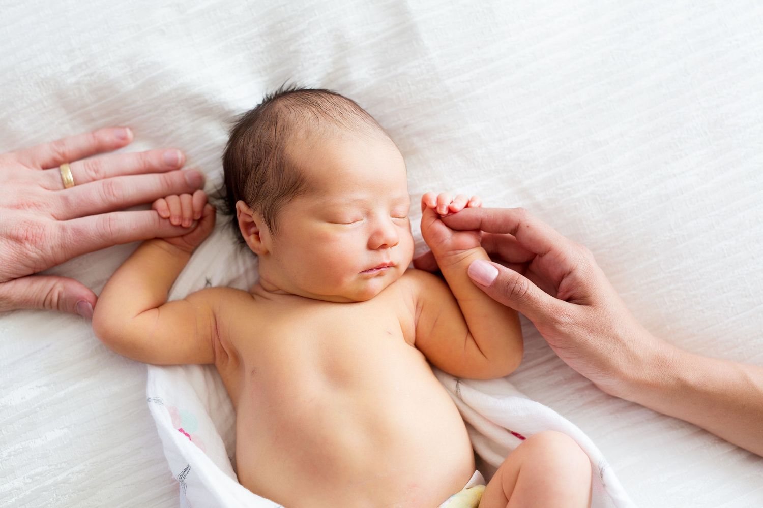 Hands gently touch sleeping newborn baby lying on white blanket.