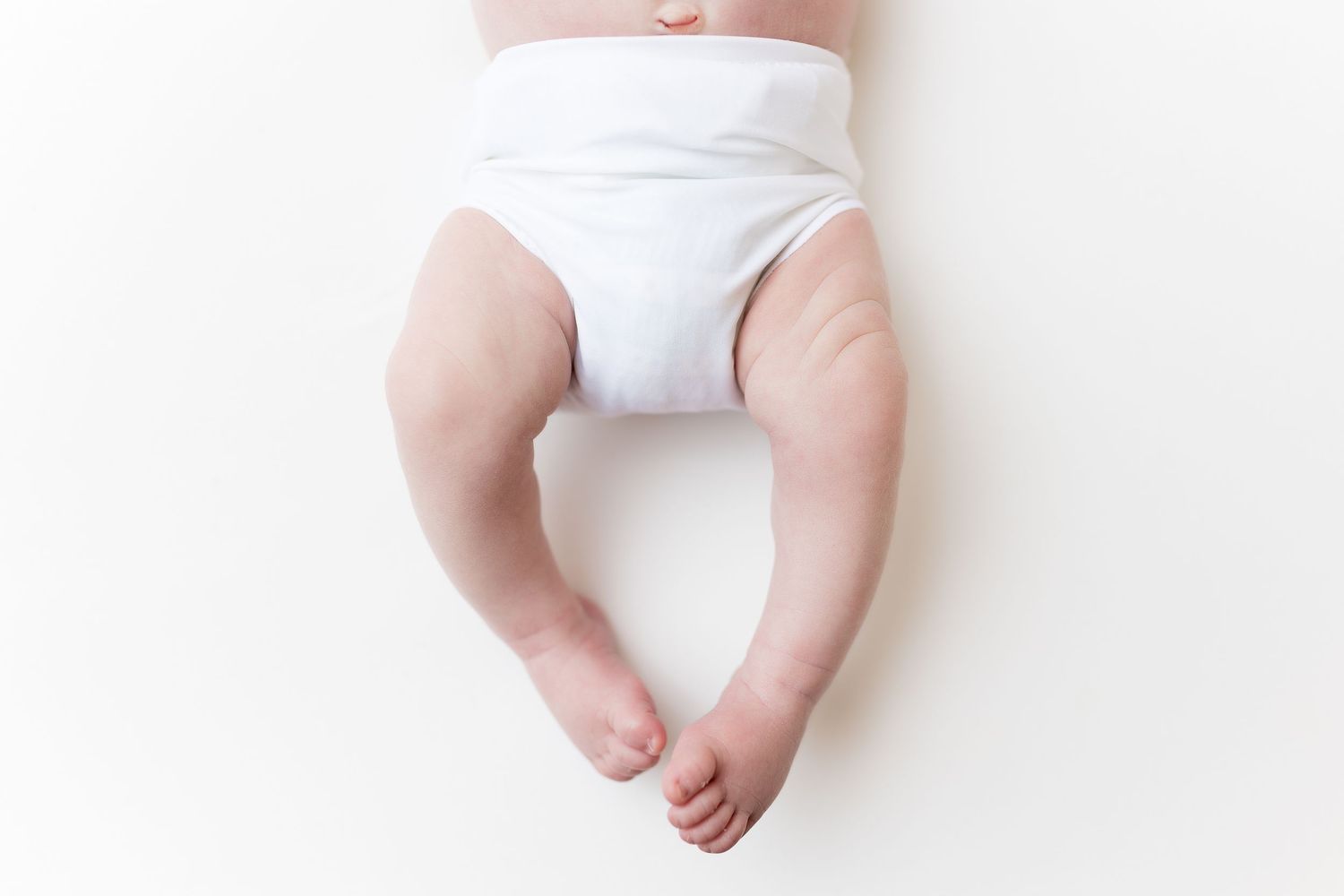 Bottom half of infant wearing white diaper against white background.