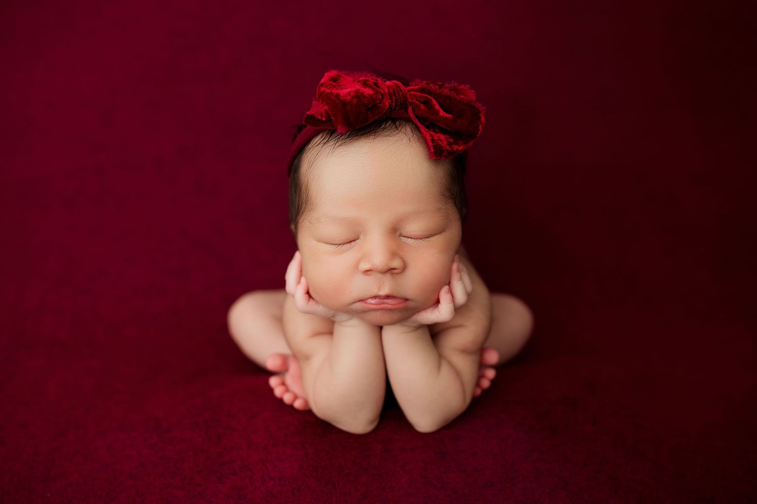 Artistic newborn portrait with deep red tones and delicate posing.