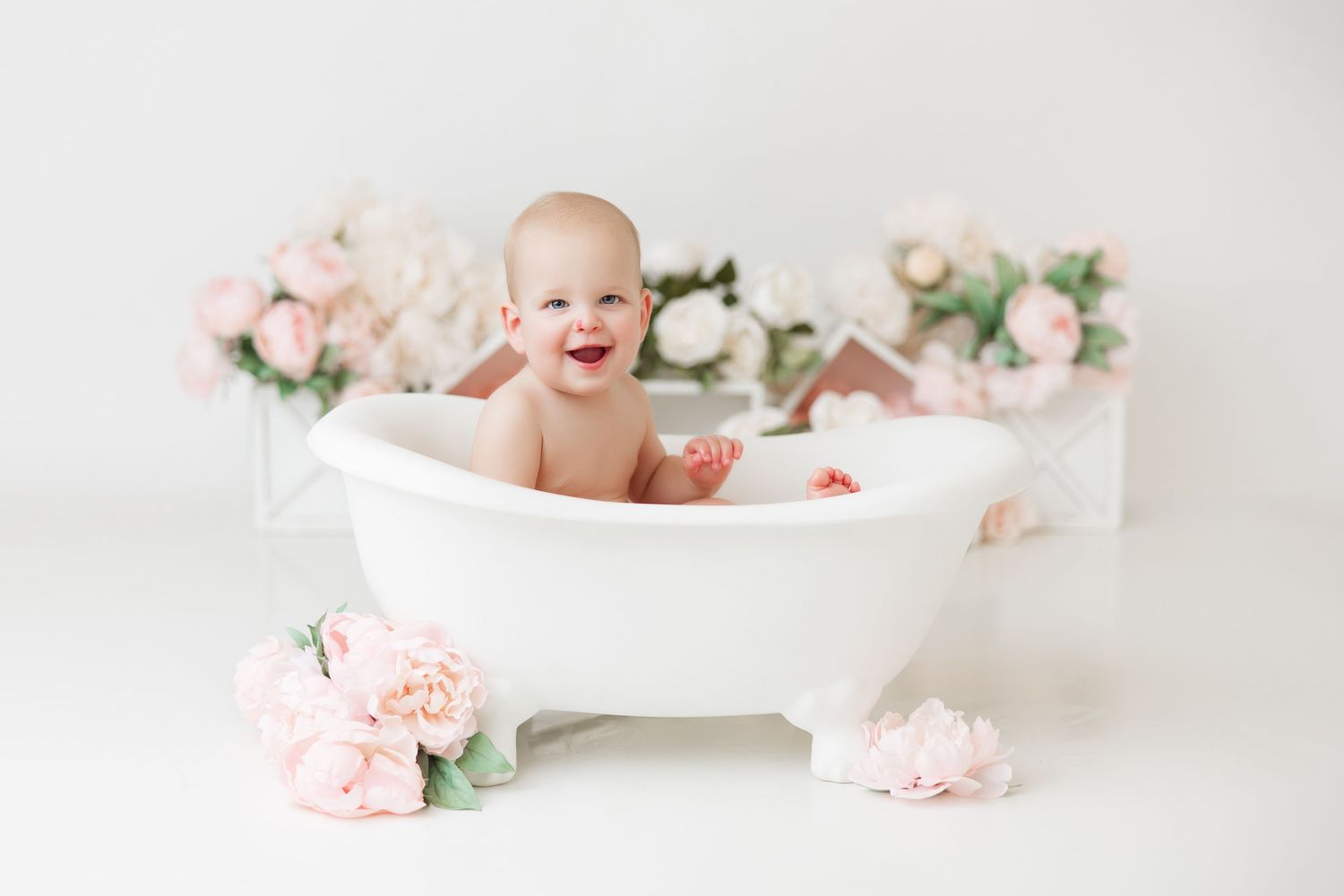 Infant posing with birthday cake surrounded by delicate pink roses.