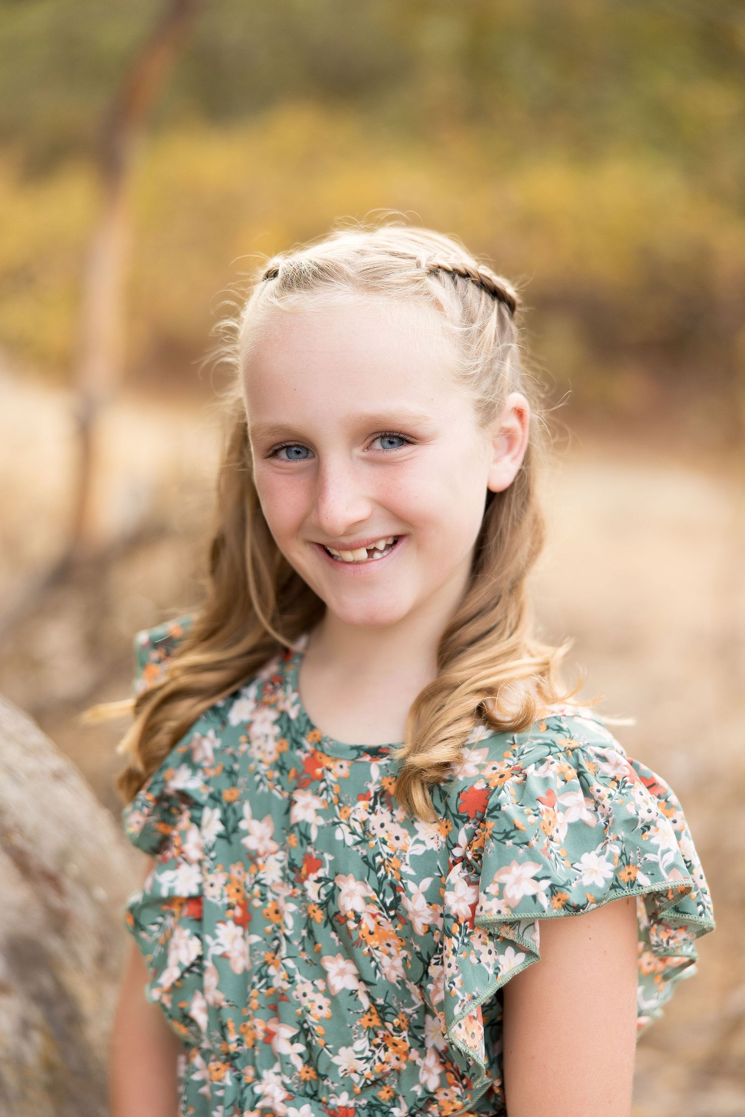 Portrait of child in floral dress with styled hair against autumn background.
