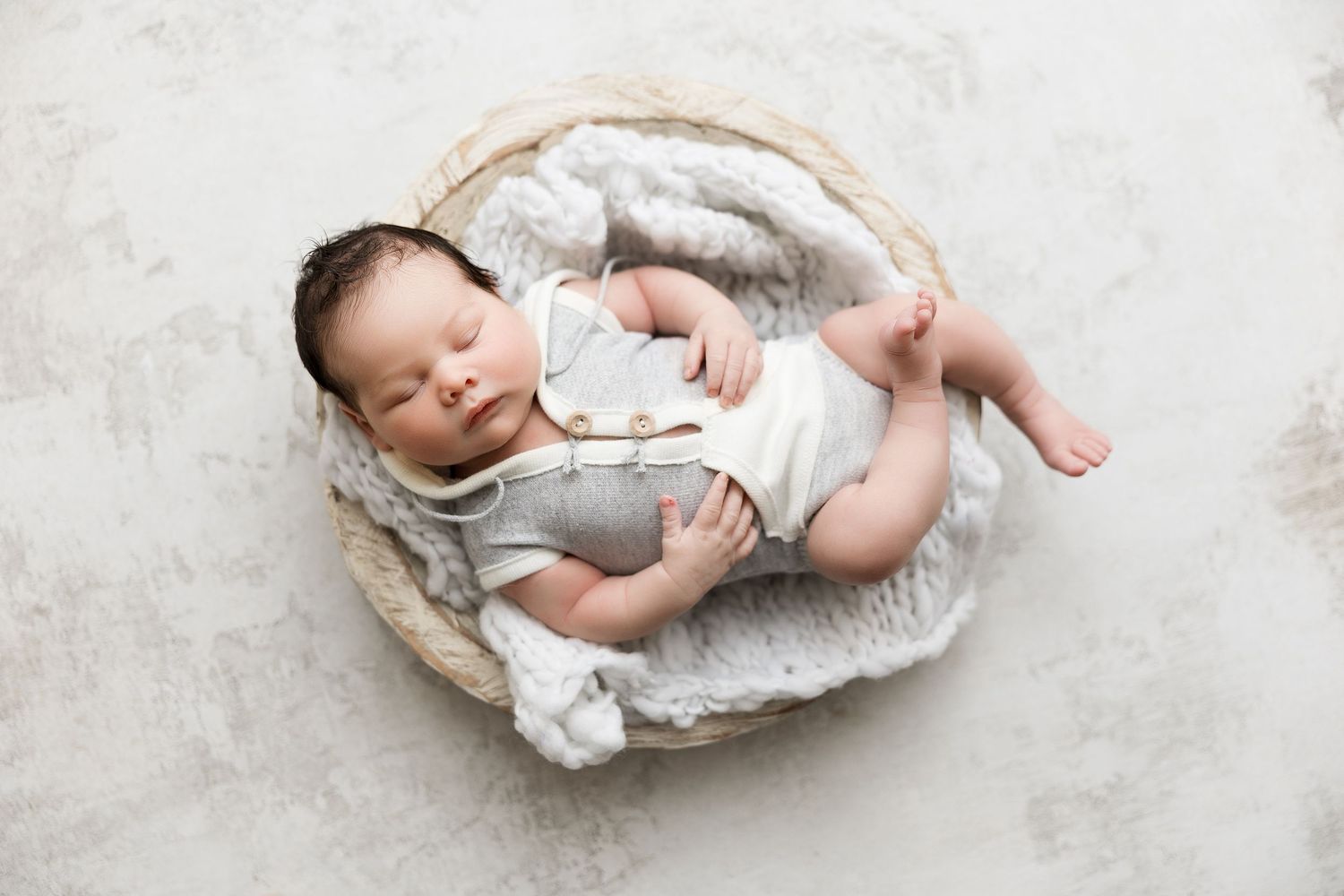 Newborn baby sleeping peacefully in white woven basket during studio photoshoot.
