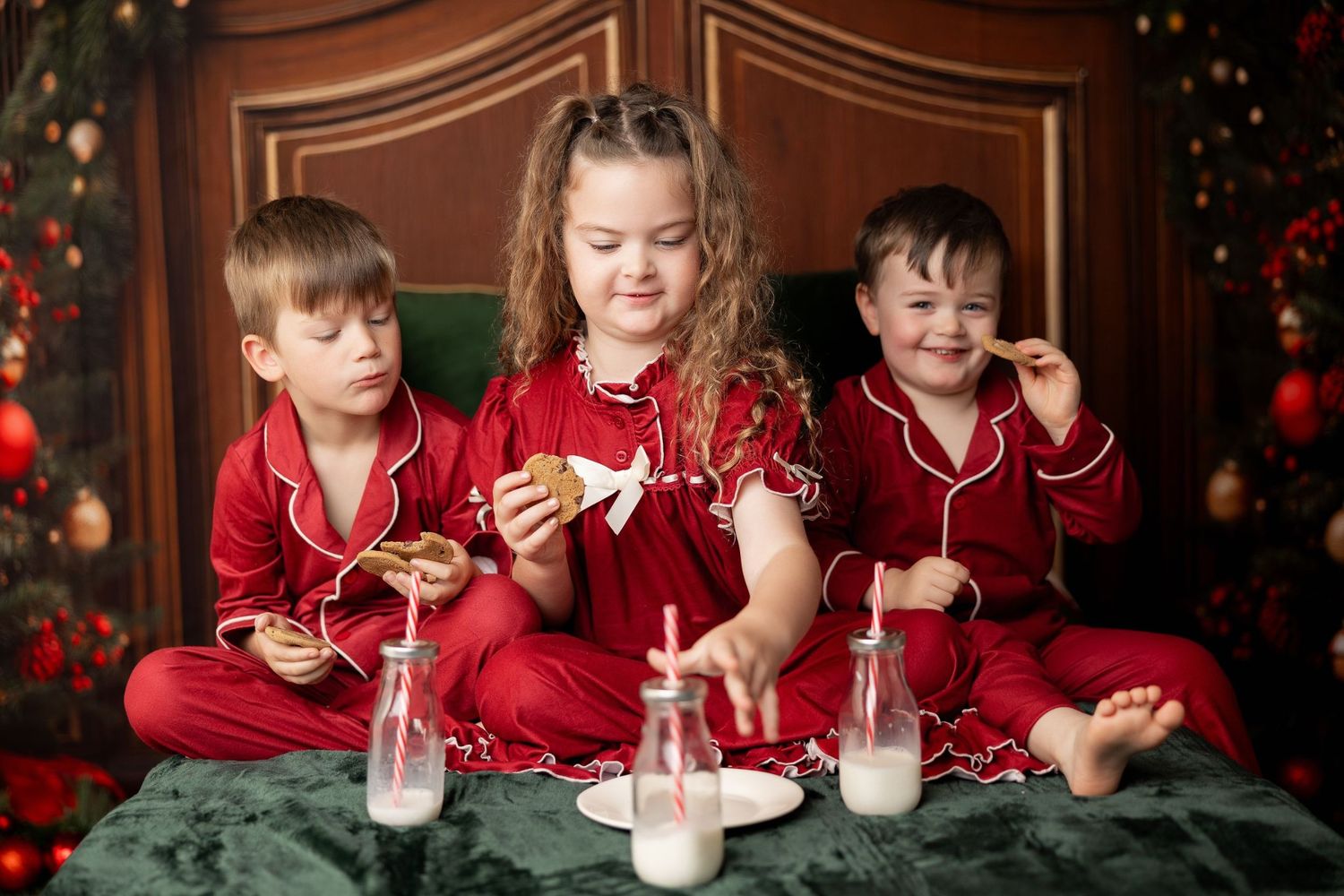 Three siblings in red Christmas pajamas enjoying milk and cookies by the tree at a holiday mini session in Pacific Grove