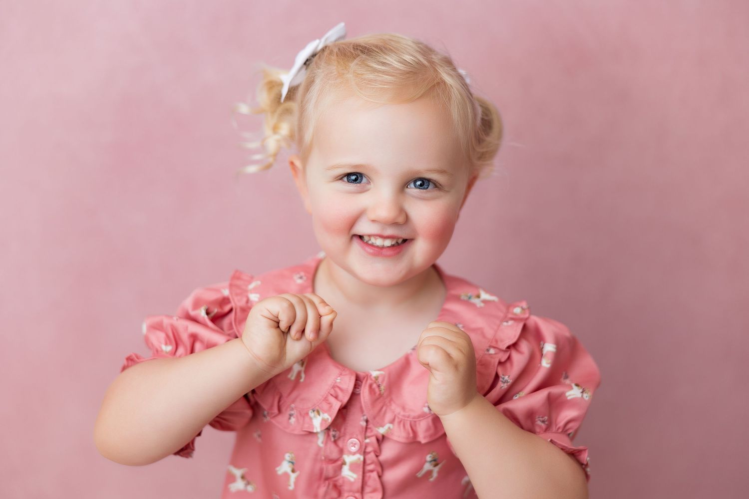 Little child wearing pink ruffled dress smiles playfully in a series of candid poses against pink backdrop.