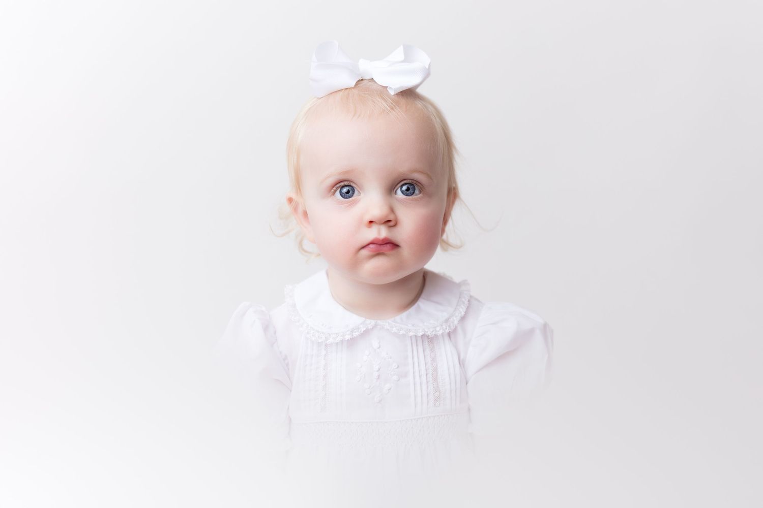 Classic baby portrait in white against minimalist light background.